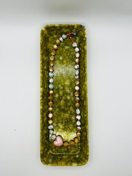 Collar Calma desplegado en bandeja rectangular verde marmolada, con chips de howlita marmolada, chips de amazonita turquesa, cuentas de coral rosa, perlas de agua dulce nacaradas y corazón central de cerámica rosa esmaltada, con cadena de extensión de acero inoxidable, hecho a mano en Murcia