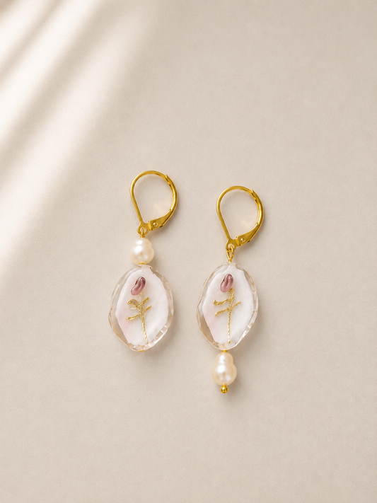 Pendientes Bella hechos a mano con flores en relieve, perlas de agua dulce y cierre dorado, sobre fondo beige.