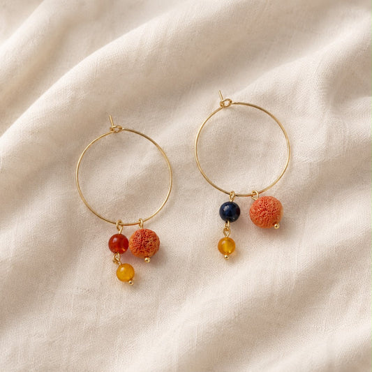 Pendientes Cala hechos a mano con aros dorados, coral, lapislázuli y ágata, fotografiados sobre tejido de lino beige.