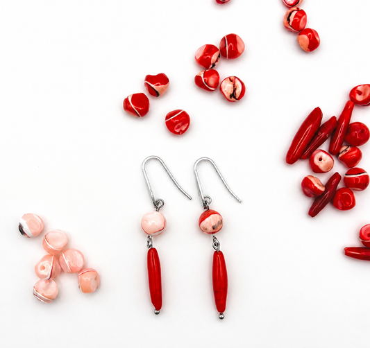 Pendientes de Cuadratura Studio con gancho de acero inoxidable plateado, cuenta de coral rosa y barra de coral rojo, rodeados de los materiales sueltos sobre fondo blanco. Montados a mano en Murcia.`