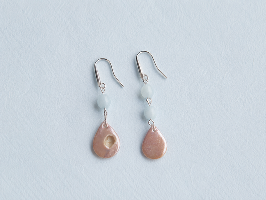 Pendientes artesanales Periwinkle con perlas nacaradas iridiscentes en forma de gota y cuentas de piedra azul, montados en acero inoxidable sobre fondo azul pastel.