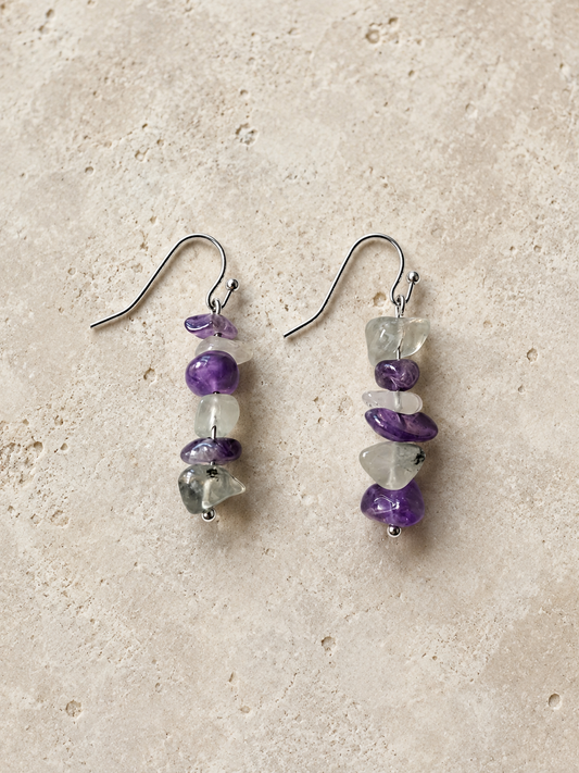 Pendientes Verena, par completo de amatista y fluorita natural en tonos violeta, blanco y verde, con gancho de acero inoxidable sobre fondo de piedra.