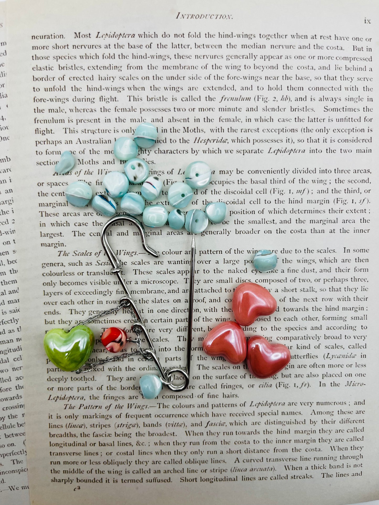 Broche Calma – imperdible plateado con semillas de rocalla azul celeste y charms de corazón de cerámica verde, rojo moteado y rosa, hecho a mano en Murcia