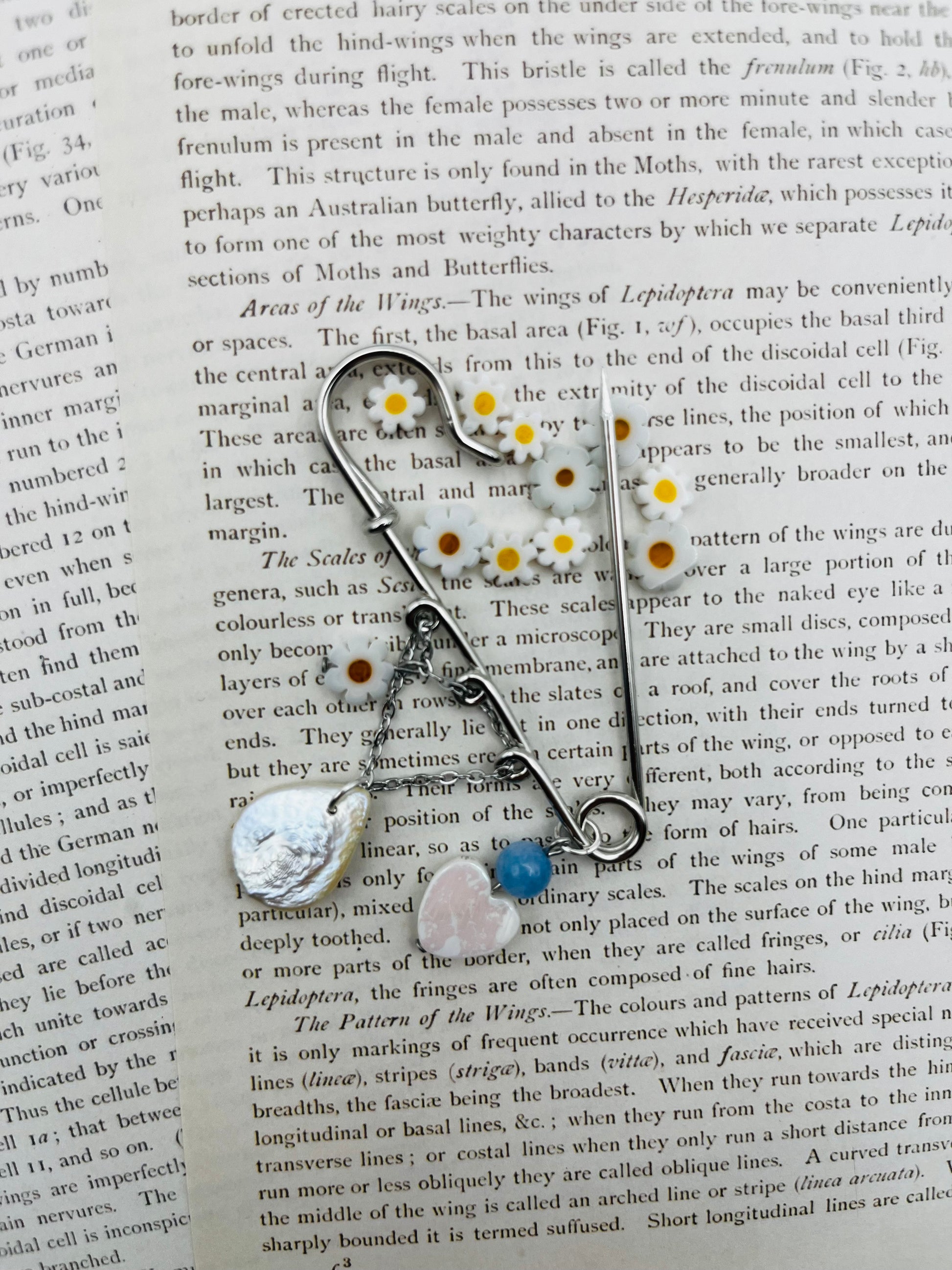 Broche Periwinkle – imperdible plateado con pieza gota de nácar, cuenta azul, corazón rosa y flores de margarita, hecho a mano en Murcia
