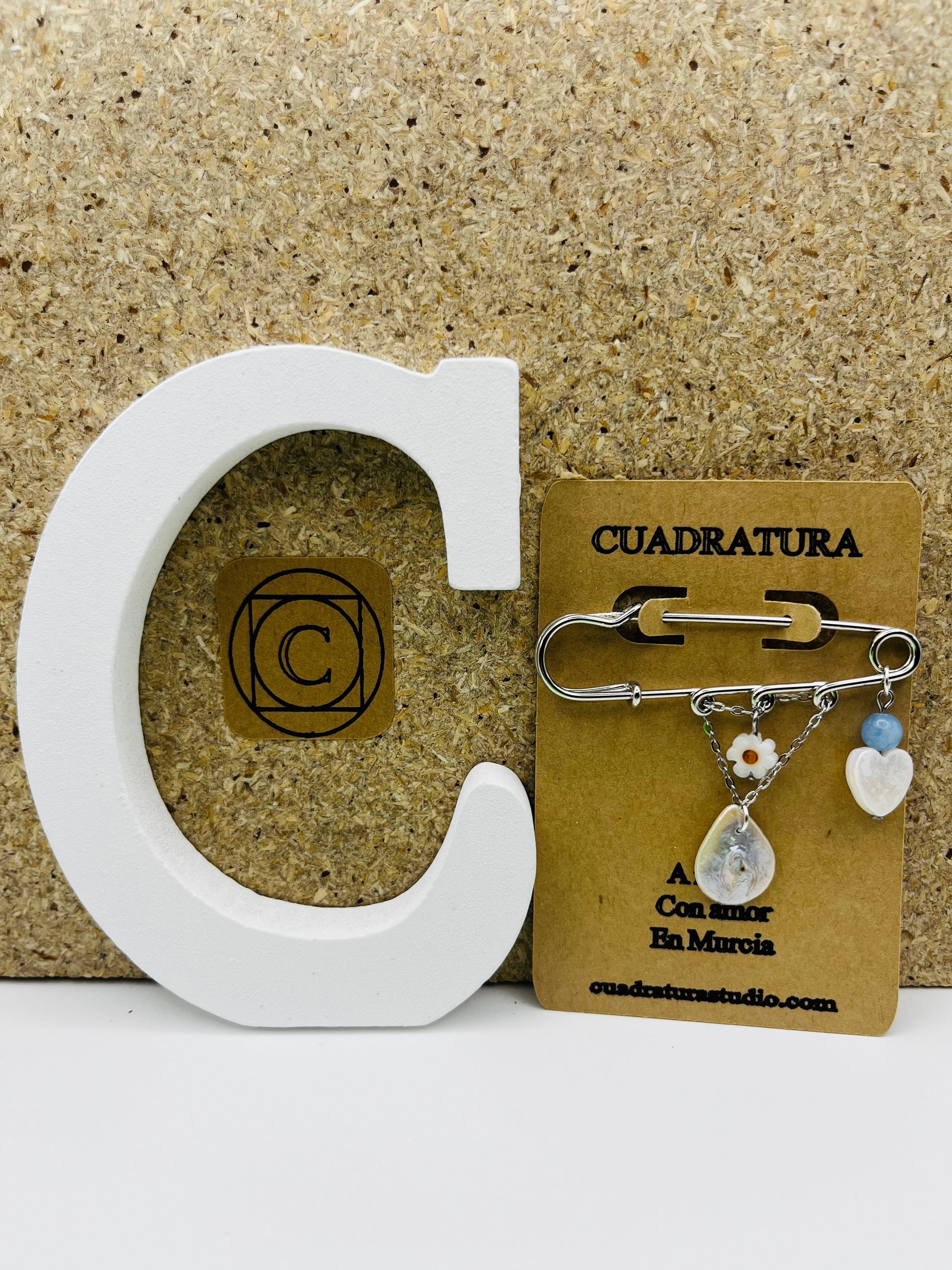 Broche Periwinkle – imperdible plateado con flor de margarita, cuenta azul, corazón de nácar y pieza gota de nácar, presentado en tarjeta Cuadratura, hecho a mano en Murcia
