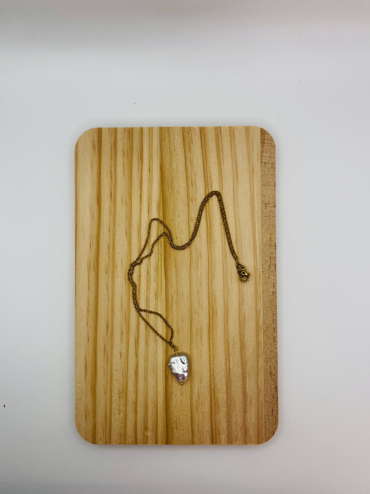 Colgante minimalista Barroca con perla keshi de agua dulce blanca en cadena fina dorada, sobre tabla de madera, montado a mano en Murcia
