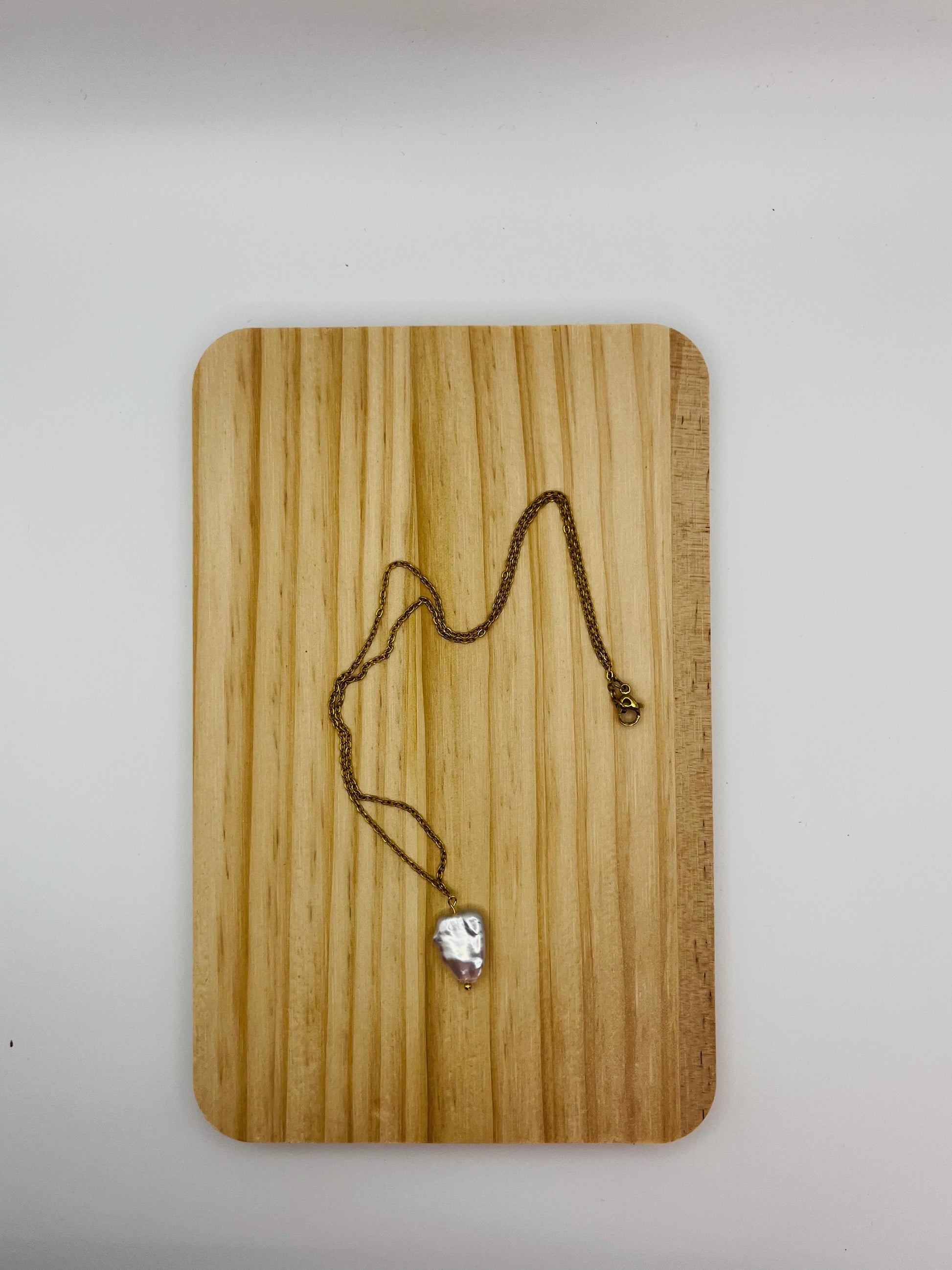 Colgante minimalista Barroca con perla keshi de agua dulce blanca en cadena fina dorada, sobre tabla de madera, montado a mano en Murcia
