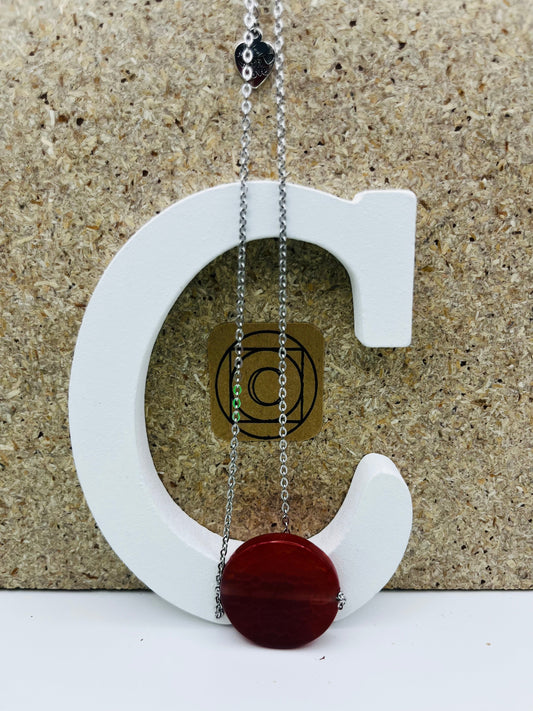 Colgante Cocedor con gran disco circular de tagua natural en rojo burdeos y charm "Made with Love" en cadena larga fina plateada, presentado sobre letra C blanca con etiqueta Cuadratura, montado a mano en Murcia
