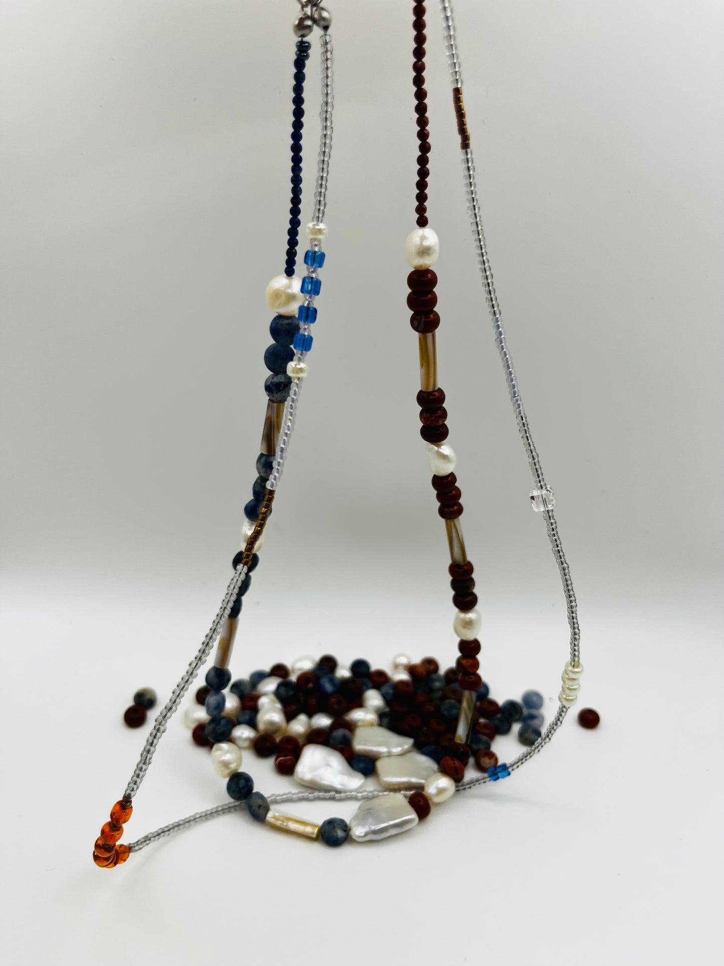 Collar Bajamar – doble collar colgado con jaspe rojo, lapislázuli azul facetado, perlas barrocas blancas, cuentas tubulares plateadas y semillas de rocalla ámbar naranja, con cuentas sueltas de jaspe y lapislázuli en el fondo, hecho a mano en Murcia