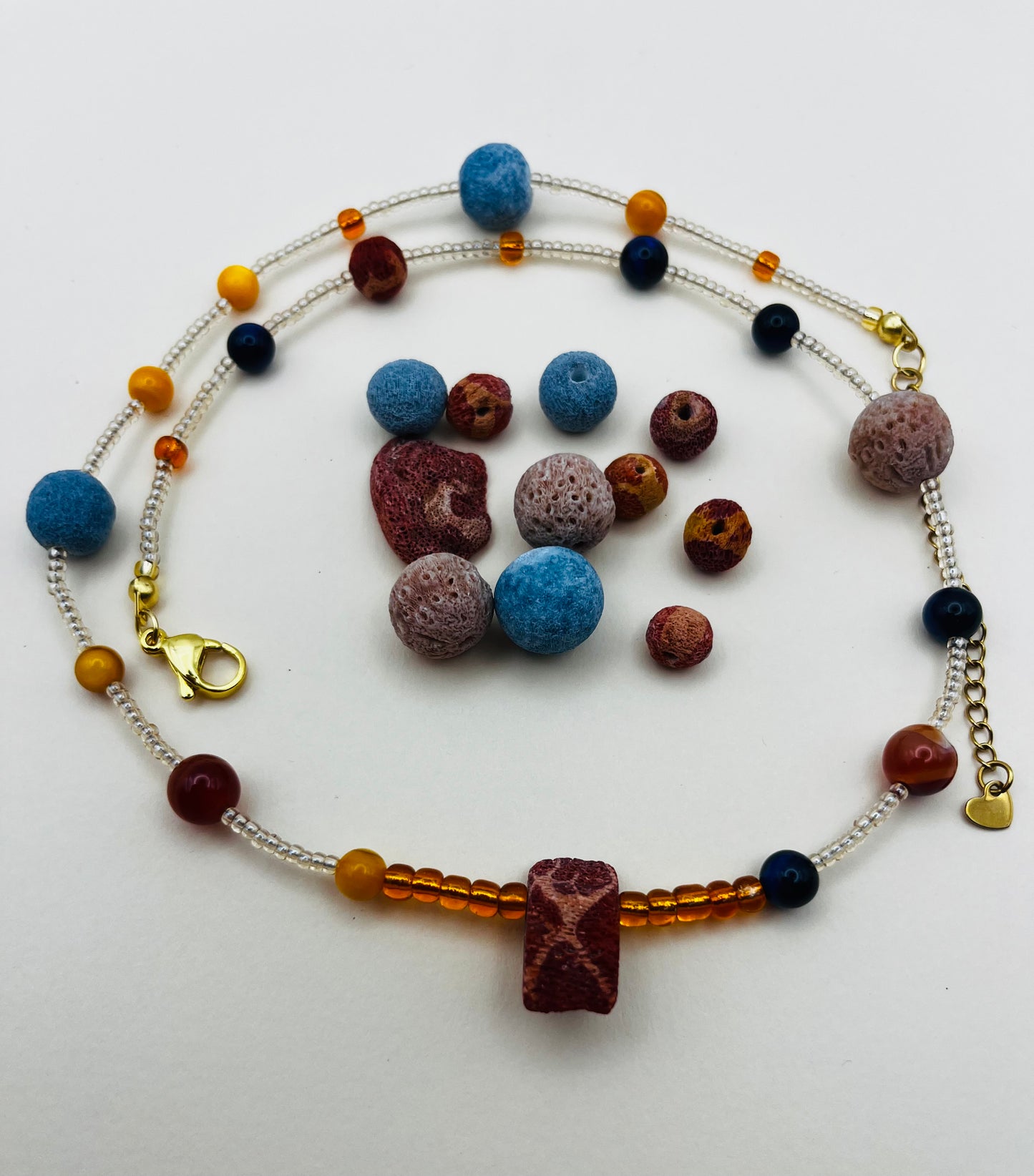 Collar Cala – semillas de rocalla transparentes con lava volcánica azul y terracota, ámbar naranja, lapislázuli azul marino y coral rojo natural, cierre dorado, hecho a mano en Murcia