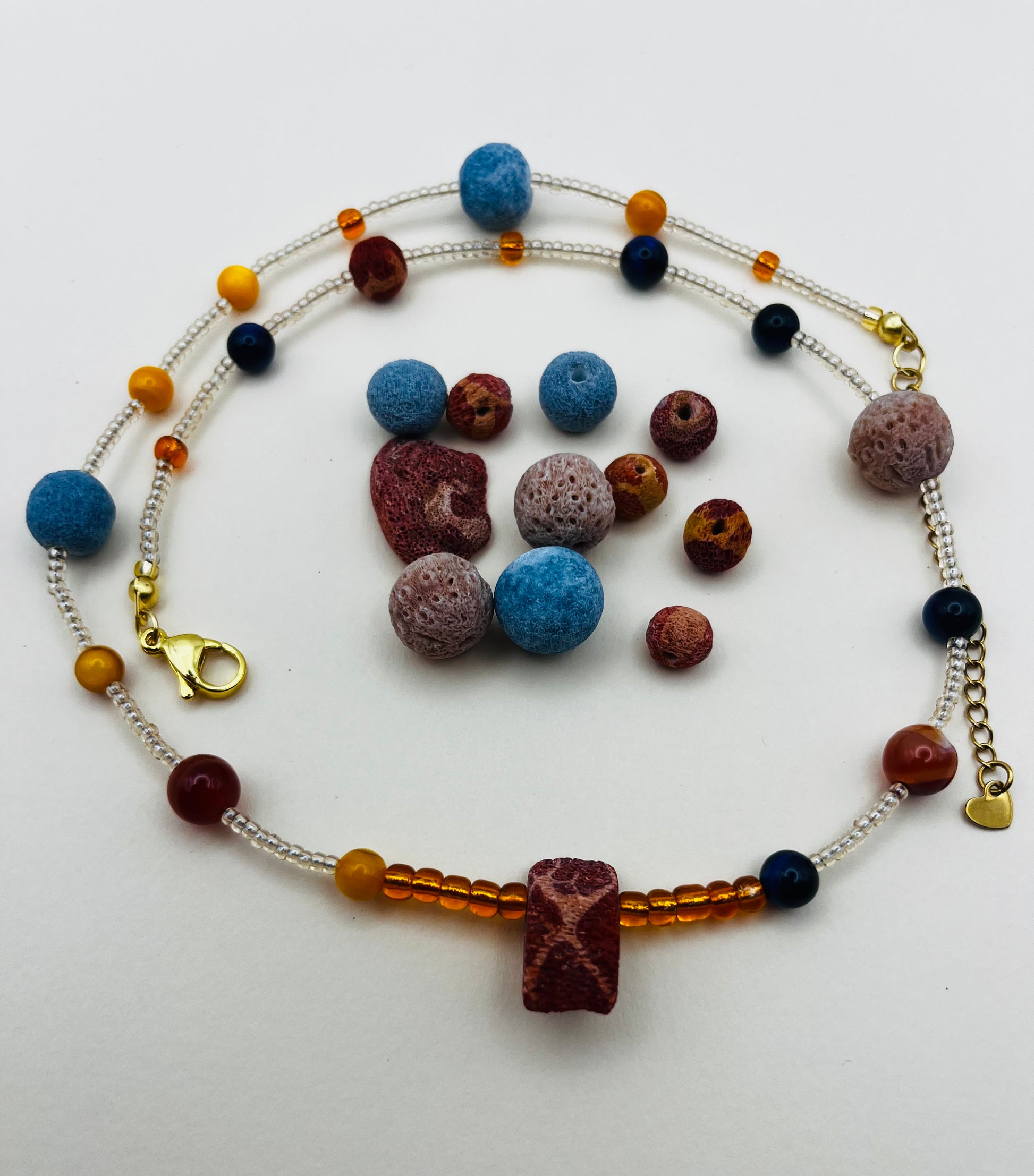 Collar Cala – semillas de rocalla transparentes con lava volcánica azul y terracota, ámbar naranja, lapislázuli azul marino y coral rojo natural, cierre dorado, hecho a mano en Murcia