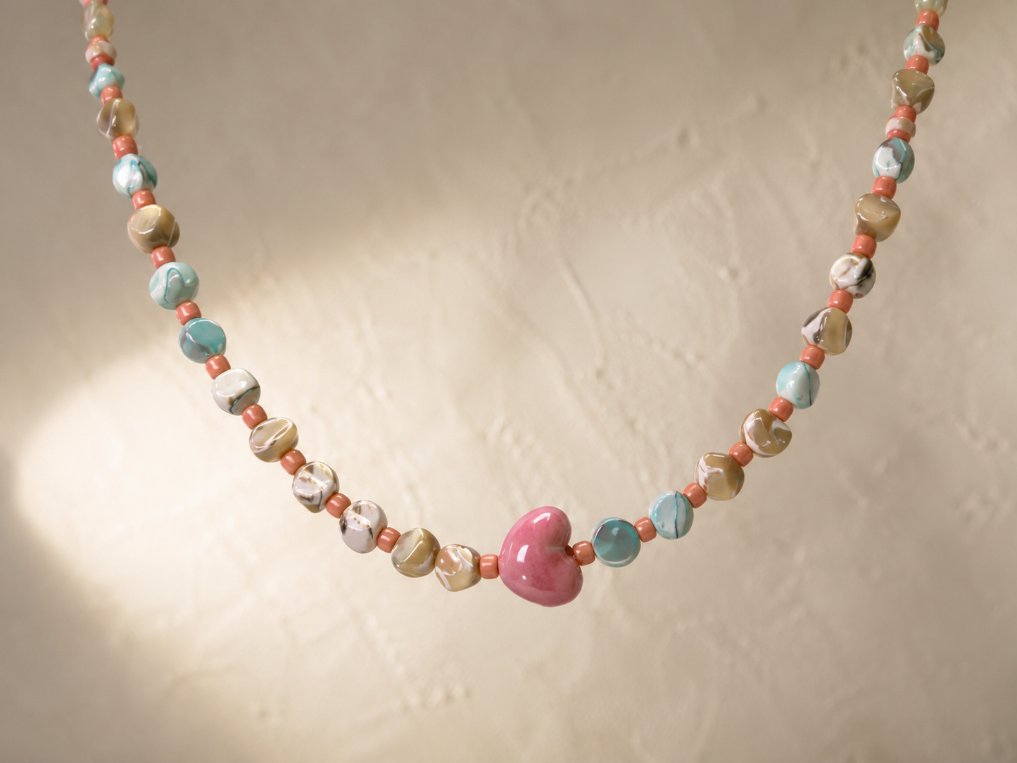 Collar Calma hecho a mano con corazón de cerámica rosa y cuentas en tonos coral, turquesa y beige.