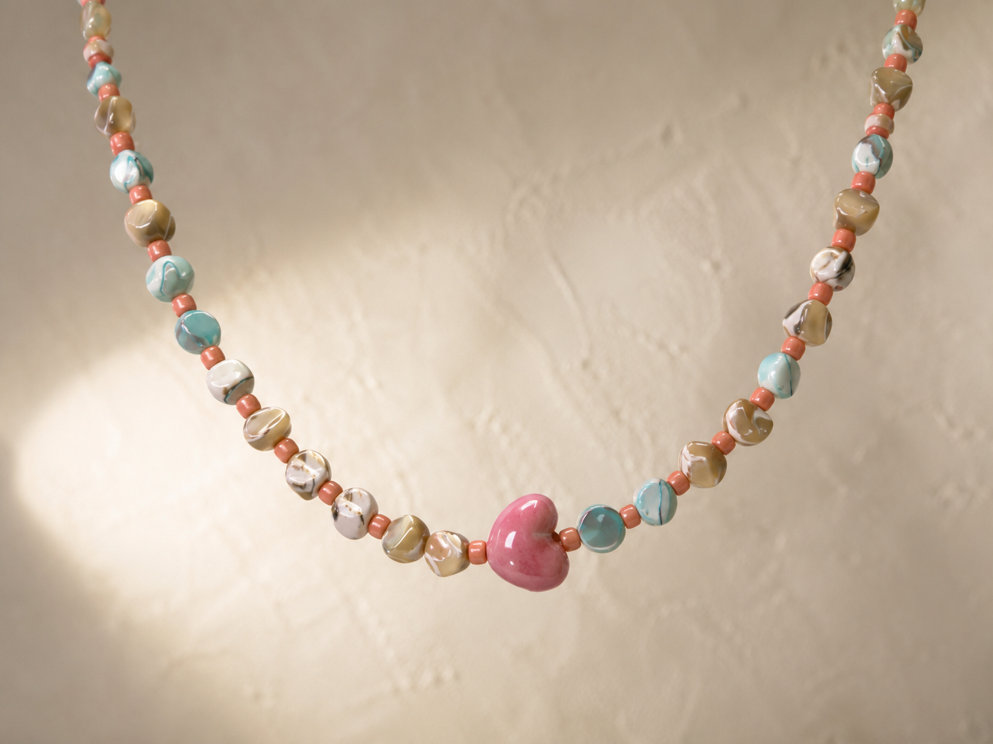 Collar Calma hecho a mano con corazón de cerámica rosa y cuentas en tonos coral, turquesa y beige.