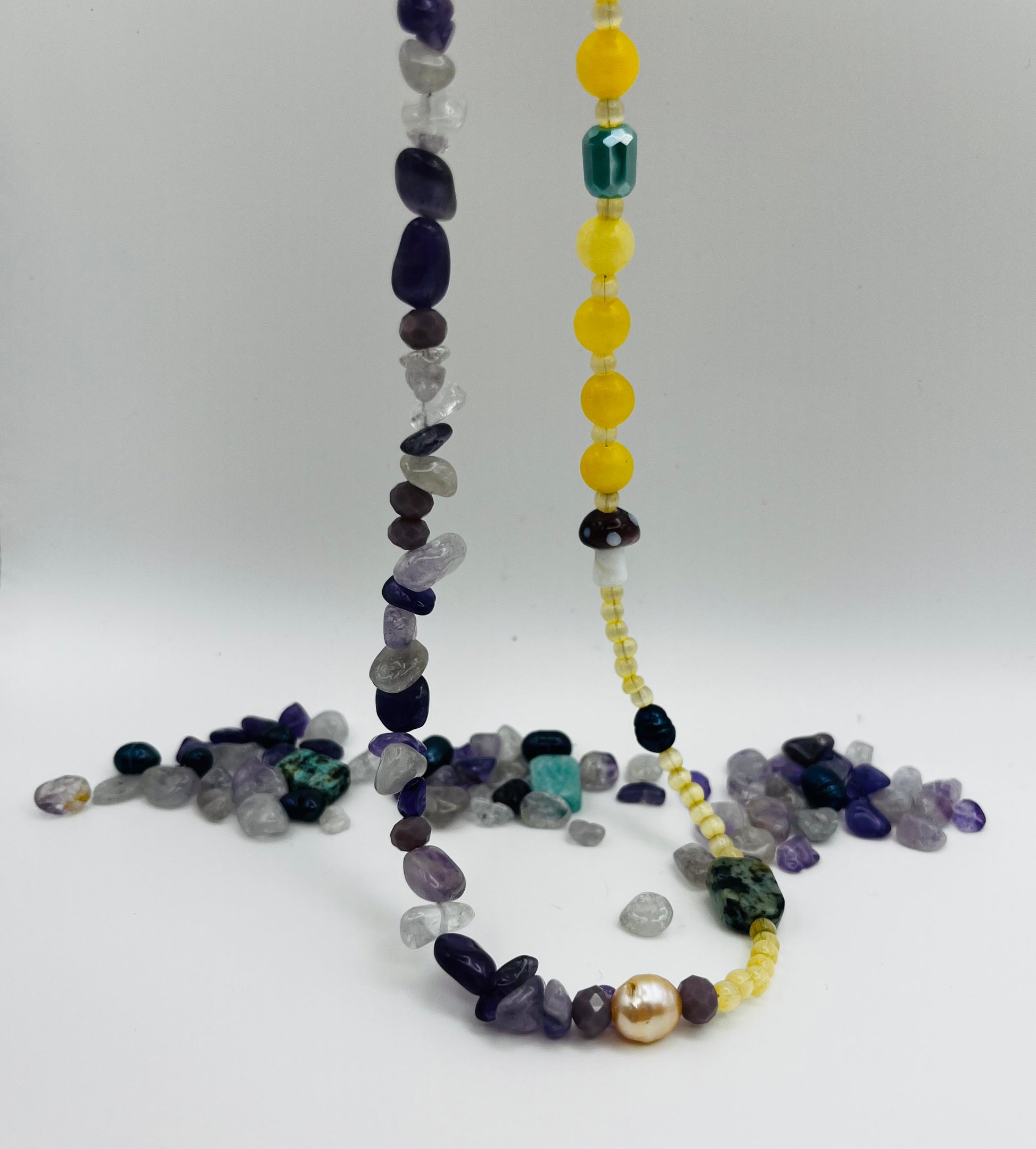 Collar Dalia – detalle del doble hilo desplegado: hilo de chips de amatista morada y lila con cuarzo, y hilo de jade amarillo con cristal verde facetado, turquesa facetada, seta de cristal morada, perla barroca amarilla y semillas de rocalla, con piedras sueltas de amatista, cuarzo y turquesa en el fondo, hecho a mano en Murcia