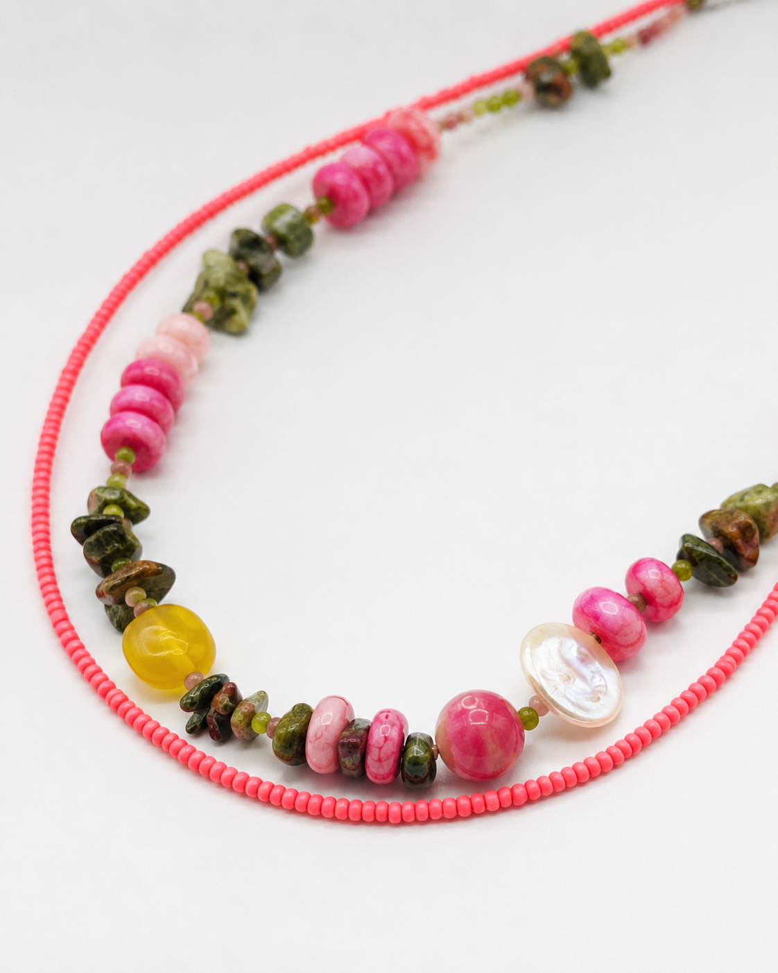 Collar Elena – detalle del doble hilo con semillas de rocalla rosas, rodocrosita rosa, chips de turmalina verde y marrón, cuenta amarilla translúcida y concha de nácar blanca, sobre fondo blanco, hecho a mano en Murcia