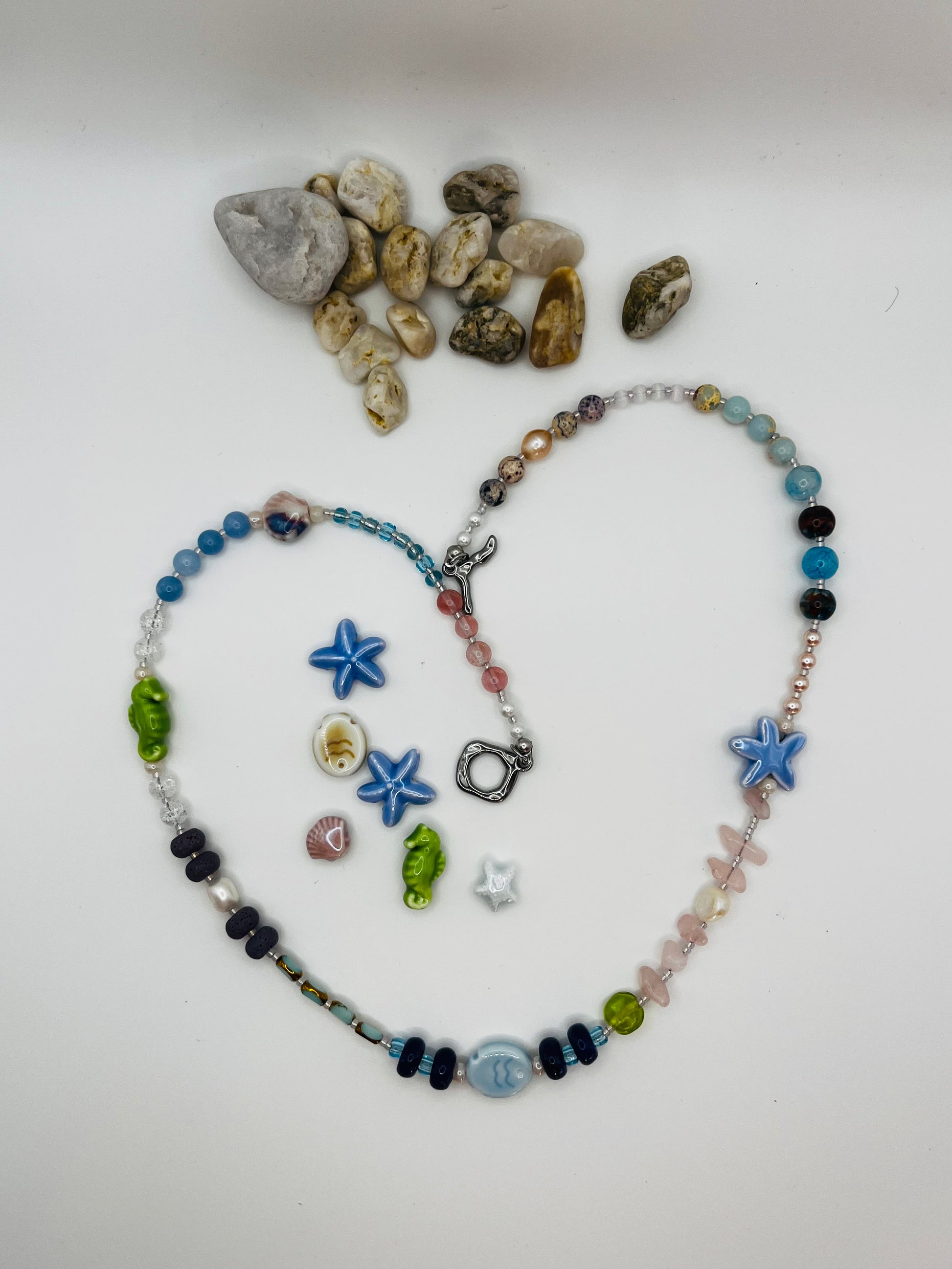 Collar Salina – collar largo con cuentas de aguamarina, cuarzo rosa, lava volcánica negra, perlas barrocas, estrella de mar y pez de cerámica azul, caballito de mar verde y cierre toggle plateado, con piezas de cerámica marina sueltas y piedras de playa, hecho a mano en Murcia