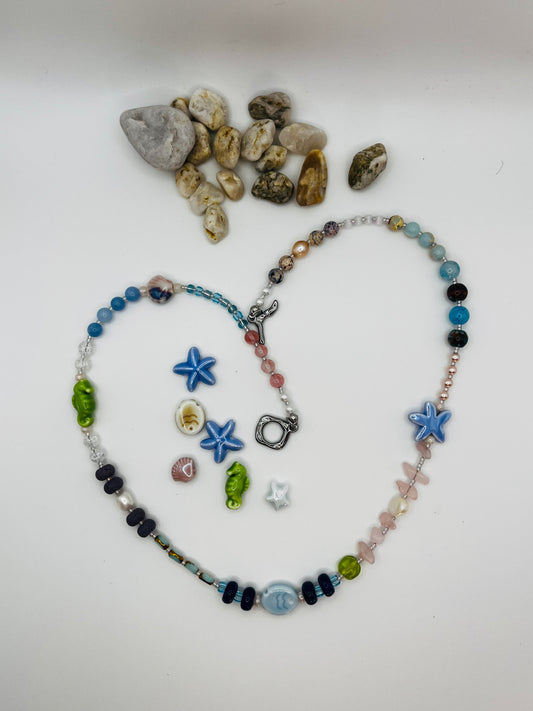 Collar Salina – collar largo con cuentas de aguamarina, cuarzo rosa, lava volcánica negra, perlas barrocas, estrella de mar y pez de cerámica azul, caballito de mar verde y cierre toggle plateado, con piezas de cerámica marina sueltas y piedras de playa, hecho a mano en Murcia