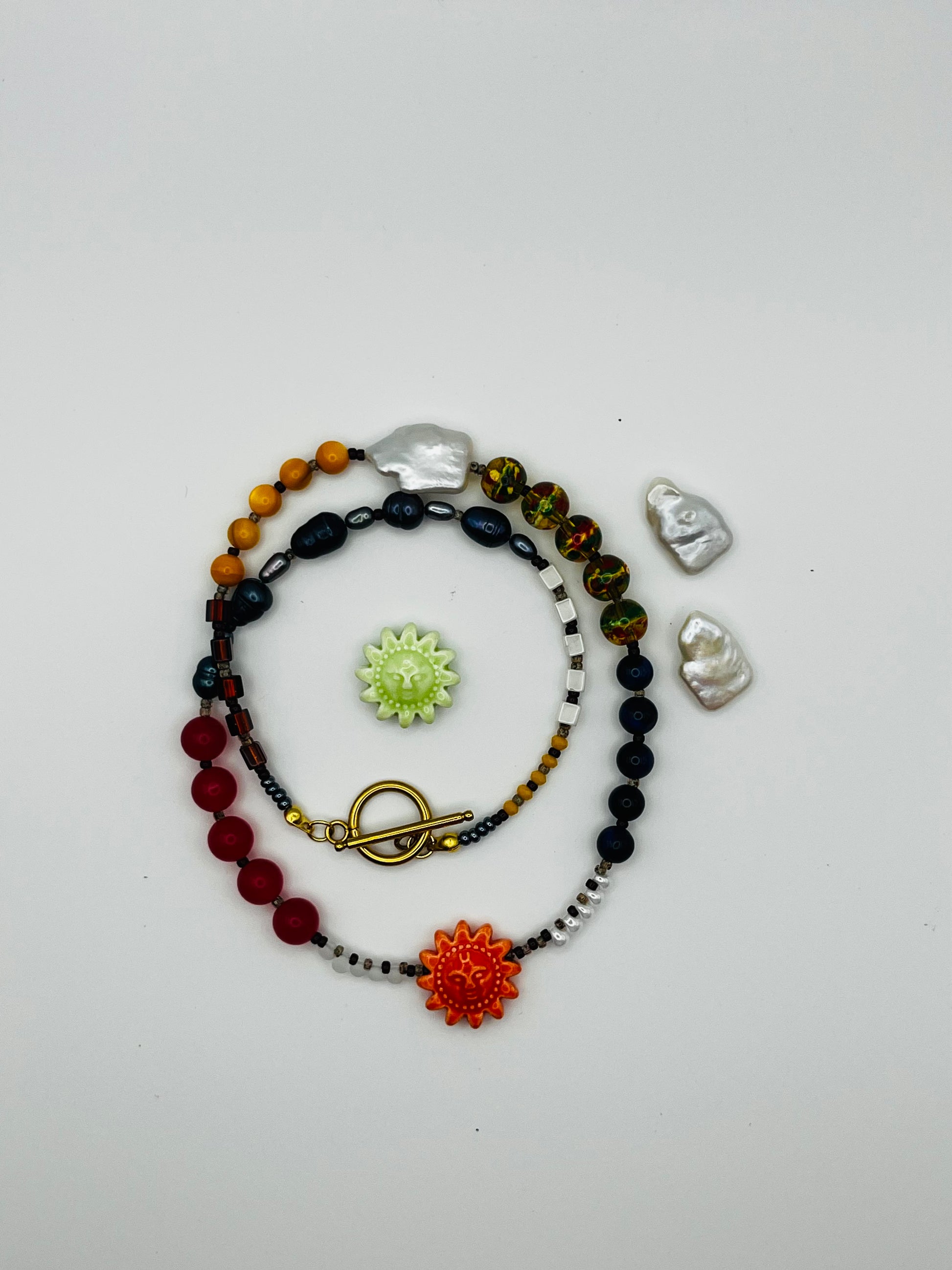 Collar Solana – collar largo enrollado con semillas de rocalla, perlas barrocas antracita, coral rojo, ágata, cloisonné, lapislázuli y sol de cerámica naranja, cierre toggle dorado, con soles de cerámica y perlas keshi sueltas, hecho a mano en Murcia