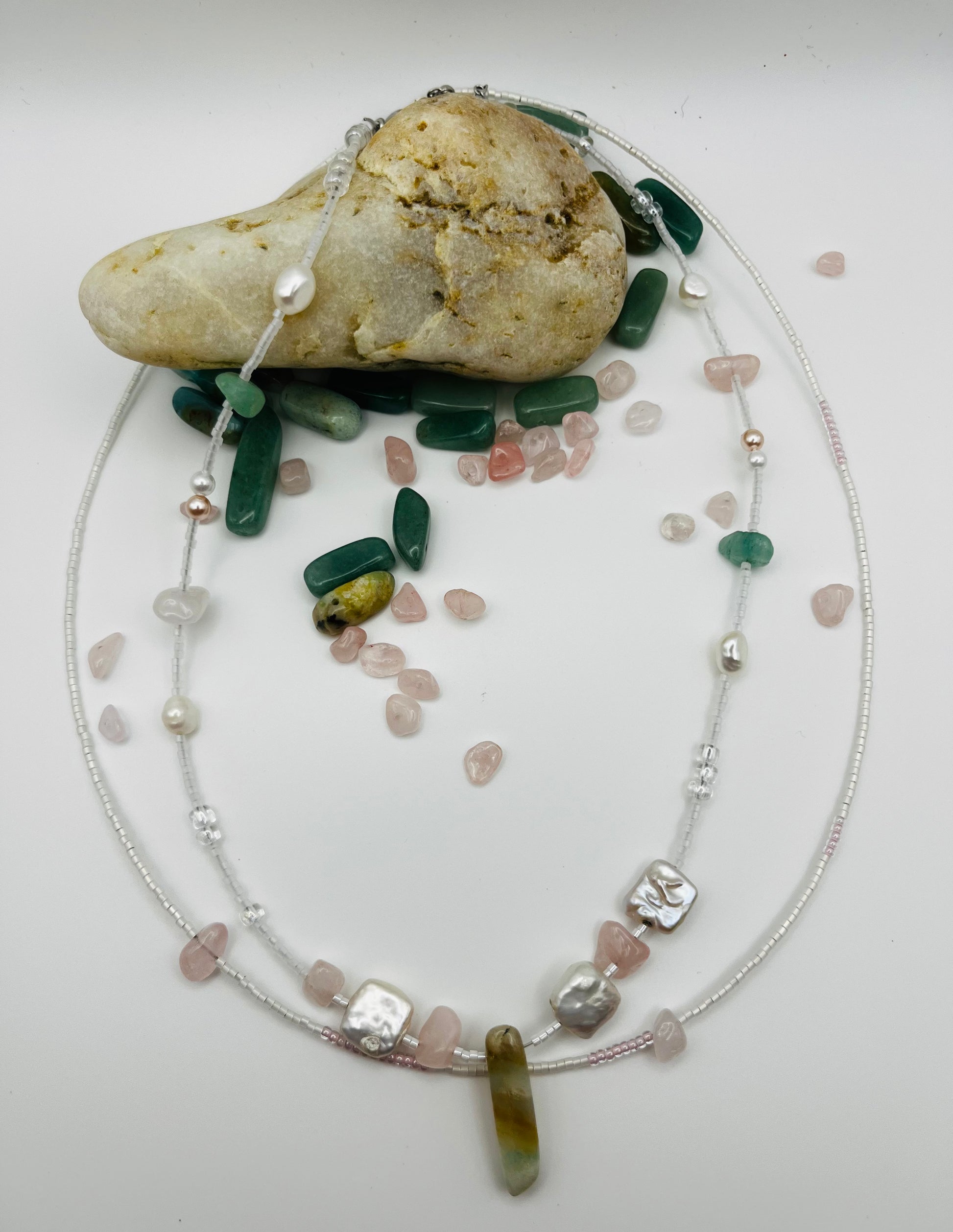 Collar Vera – doble collar desplegado con semillas de rocalla blancas y transparentes, perlas barrocas cuadradas blancas, chips de cuarzo rosa, bolitas plateadas y cuenta alargada de jade verde oliva, con chips de jade verde y cuarzo rosa sueltos esparcidos y piedra de playa, hecho a mano en Murcia