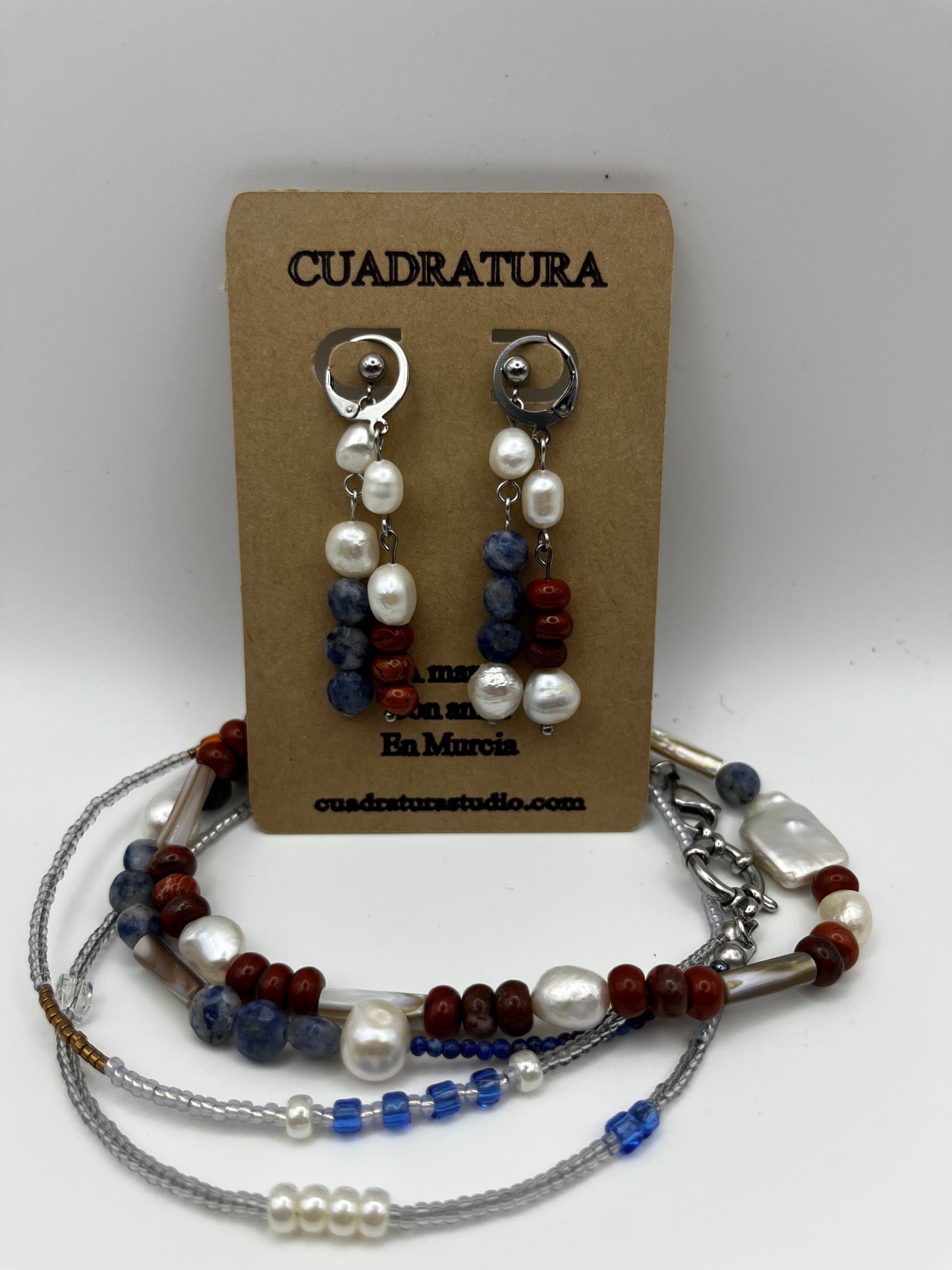 Conjunto Bajamar – collar doble con jaspe rojo, lapislázuli azul, perlas barrocas blancas y semillas de rocalla ámbar, junto a Pendientes Bajamar con perlas keshi y lapislázuli, en tarjeta Cuadratura, hechos a mano en Murcia