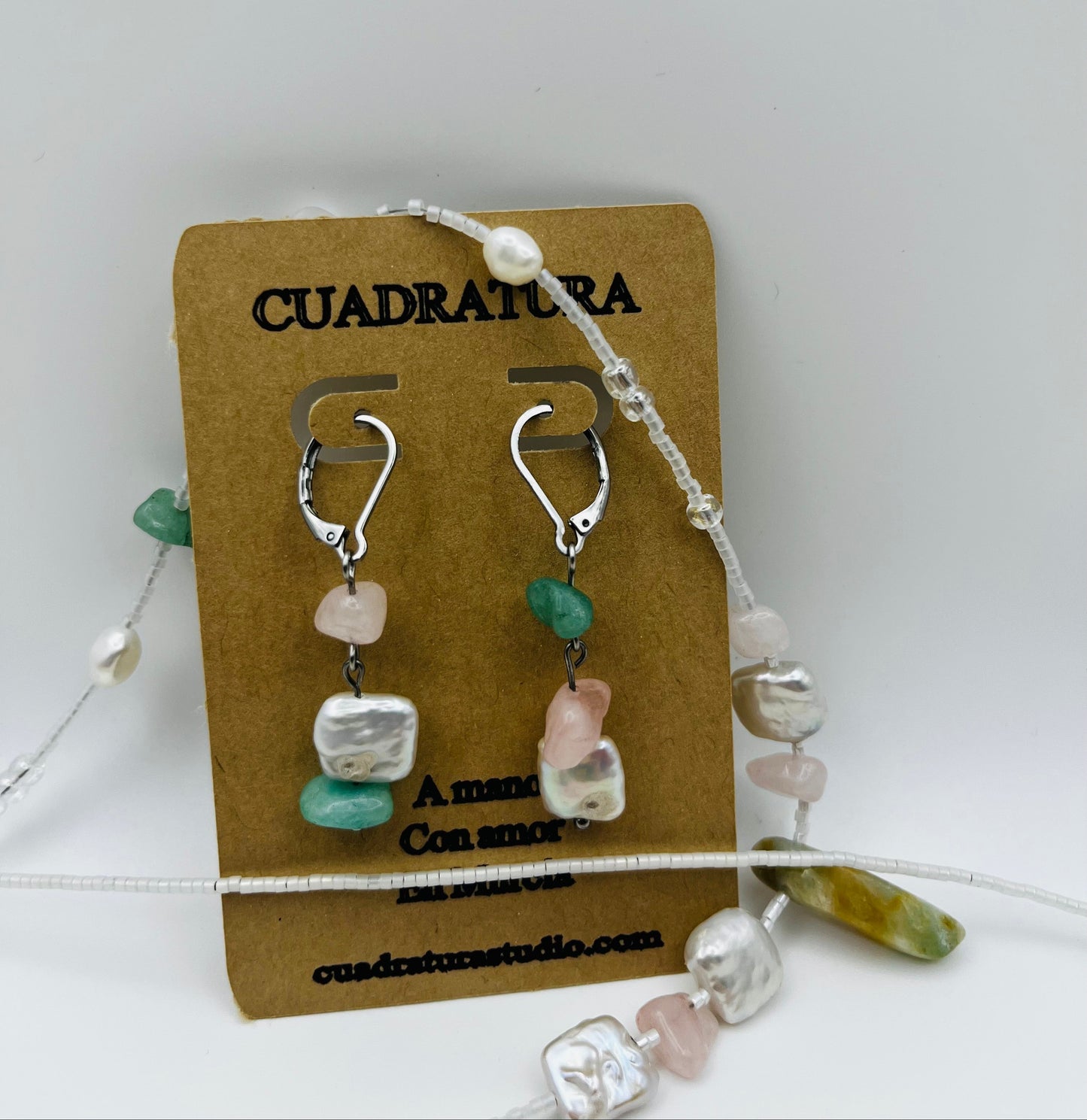 Conjunto Vera – Pendientes Vera asimétricos con aro plateado, chip de cuarzo rosa, chip de jade verde, perla barroca cuadrada blanca y chip de amazonita, en tarjeta Cuadratura, con Collar Vera de doble hilo desplegado alrededor, hechos a mano en Murcia