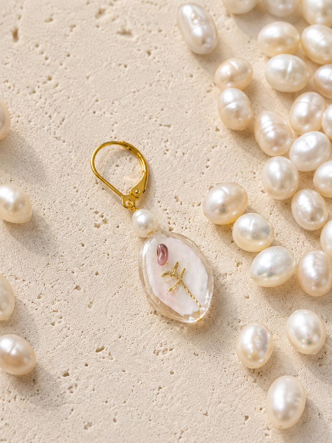 Pendiente Bella hecho a mano con flor en relieve, perla de agua dulce y cierre dorado, rodeado de perlas sobre fondo de piedra.