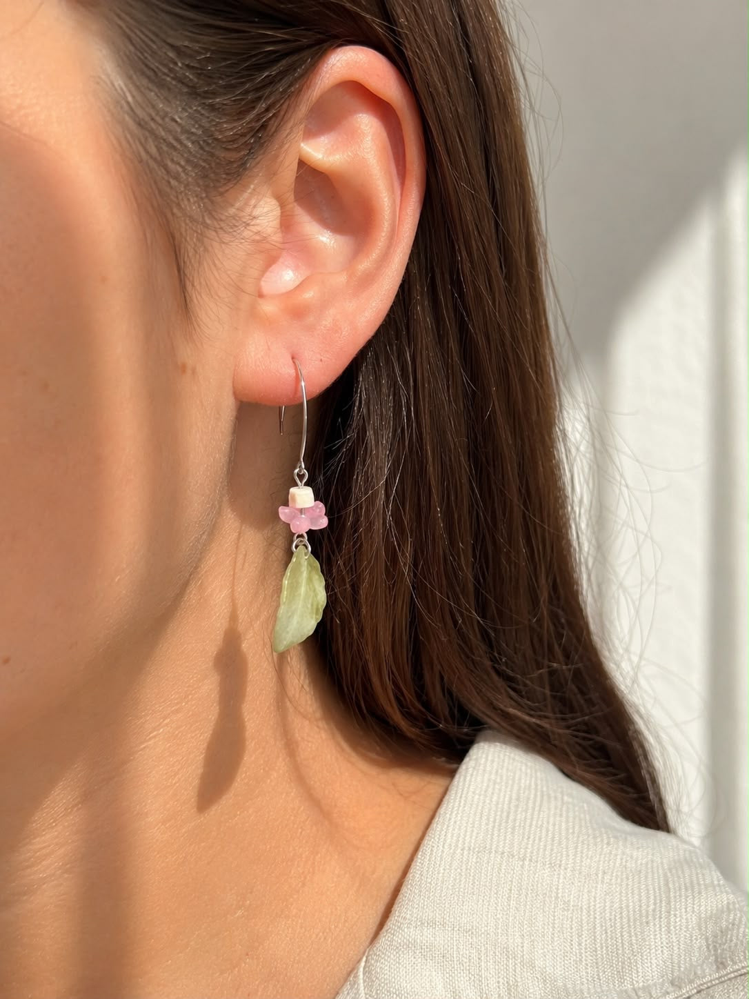 Mujer luciendo un pendiente Primavera hecho a mano con hoja de jade tallado, flor de cristal rosa y cierre plateado.