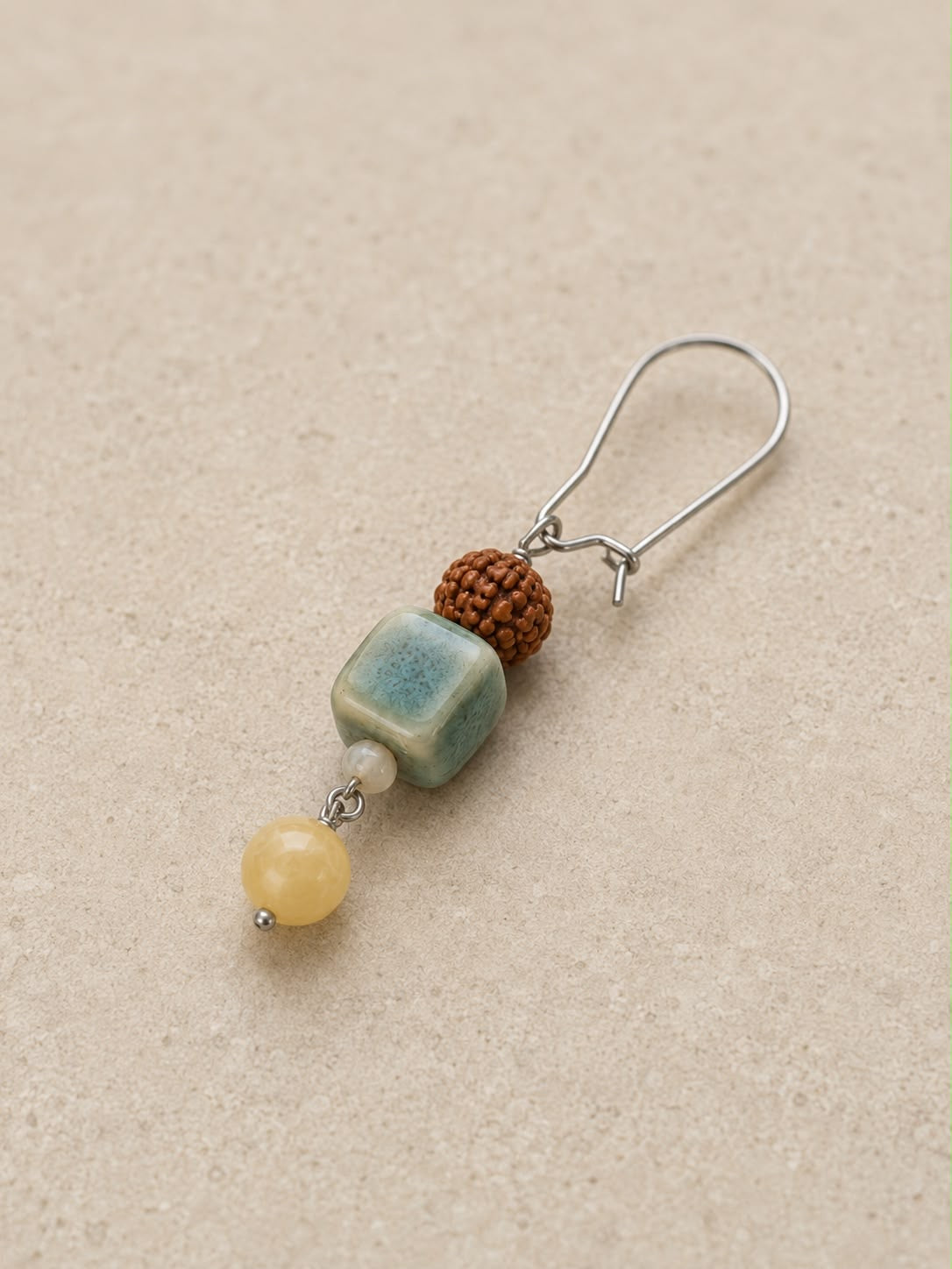 Pendiente Siena individual en vista alternativa con cerámica artesanal verde, jade amarillo, cuenta de rudraksha y cierre plateado.