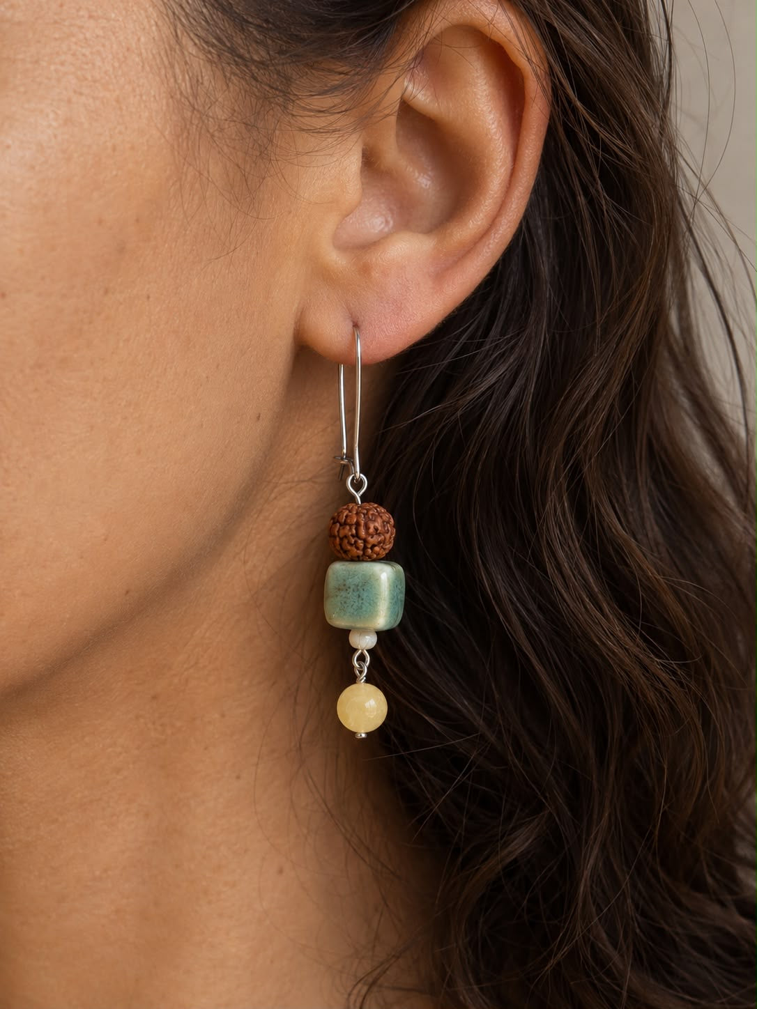 Mujer luciendo un pendiente Siena hecho a mano con cerámica artesanal verde, jade amarillo, cuenta de rudraksha y cierre plateado.