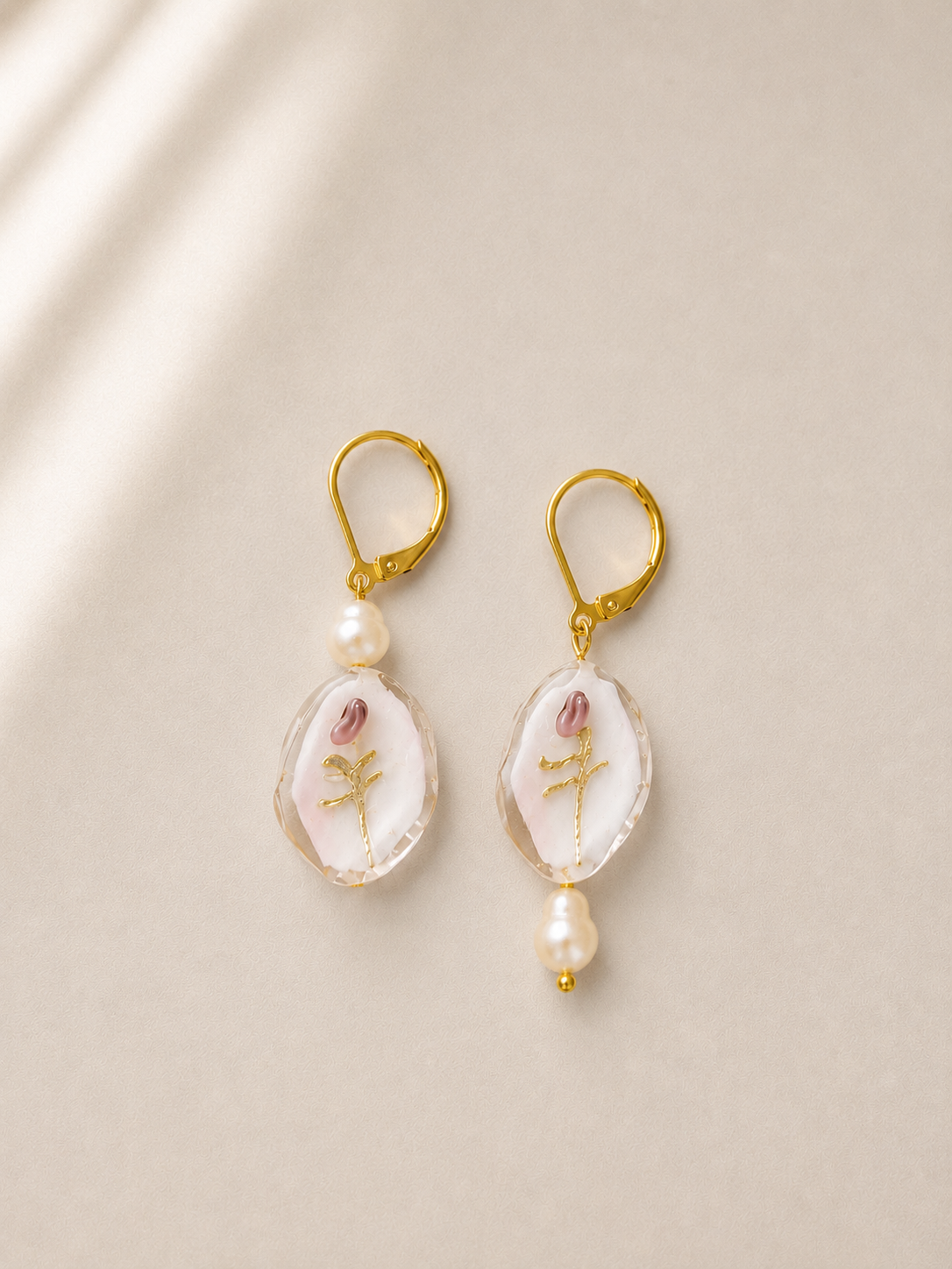 Pendientes Bella hechos a mano con flores en relieve, perlas de agua dulce y cierre dorado, sobre fondo beige.