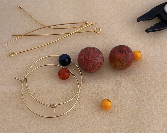 Componentes de los pendientes Cala dispuestos para su elaboración artesanal, con aros dorados, coral, lapislázuli y ágata.