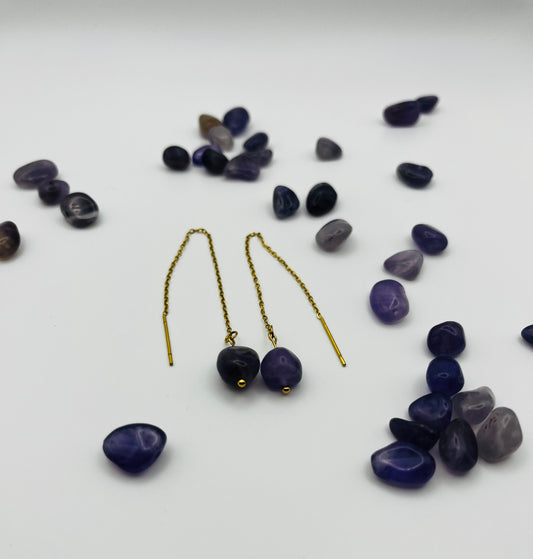 Pendientes Délica – pendientes simétricos con gancho threader dorado, cadena dorada fina y cuenta ovalada de amatista morada oscura natural, con cuentas de amatista morada de distintos tonos sueltas esparcidas, sobre fondo blanco, hechos a mano en Murcia