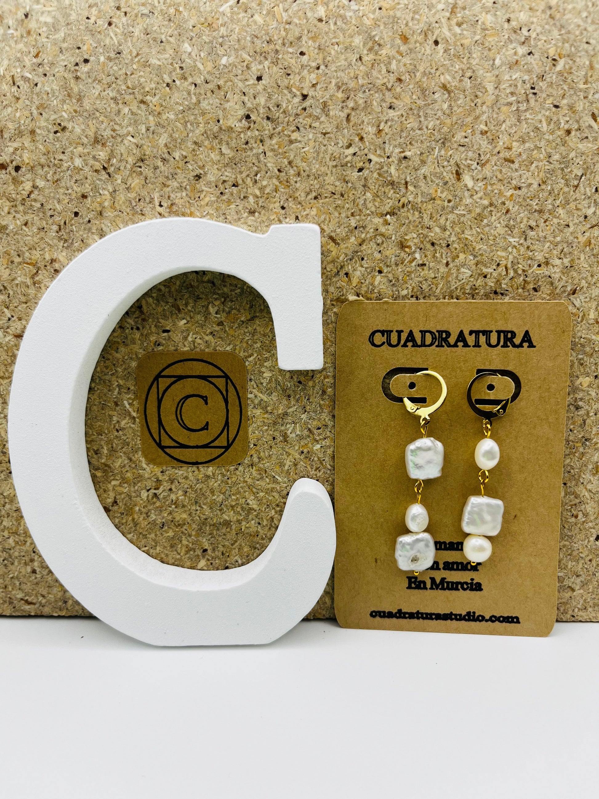 Pendientes Espuma – pendientes asimétricos con aro dorado, perla barroca cuadrada blanca, perla barroca ovalada blanca y perla barroca rectangular blanca de agua dulce, en tarjeta Cuadratura, sobre letra C blanca y fondo de corcho, hechos a mano en Murcia