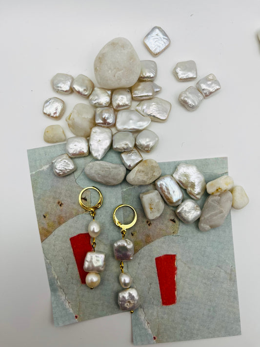 Pendientes Espuma – pendientes con aro dorado y tres perlas barrocas de agua dulce blancas en cadena (keshi, ovalada y cuadrada), sobre papel de acuarela azul grisáceo con perlas barrocas cuadradas sueltas y piedras de playa blancas esparcidas, hechos a mano en Murcia