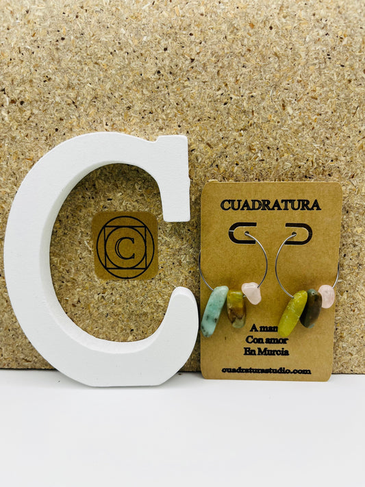 Pendientes Levante – pendientes asimétricos con aro plateado fino y chips de amazonita turquesa, jade verde oliva, cuarzo rosa y jaspe marrón, en tarjeta Cuadratura, sobre letra C blanca y fondo de corcho, hechos a mano en Murcia
