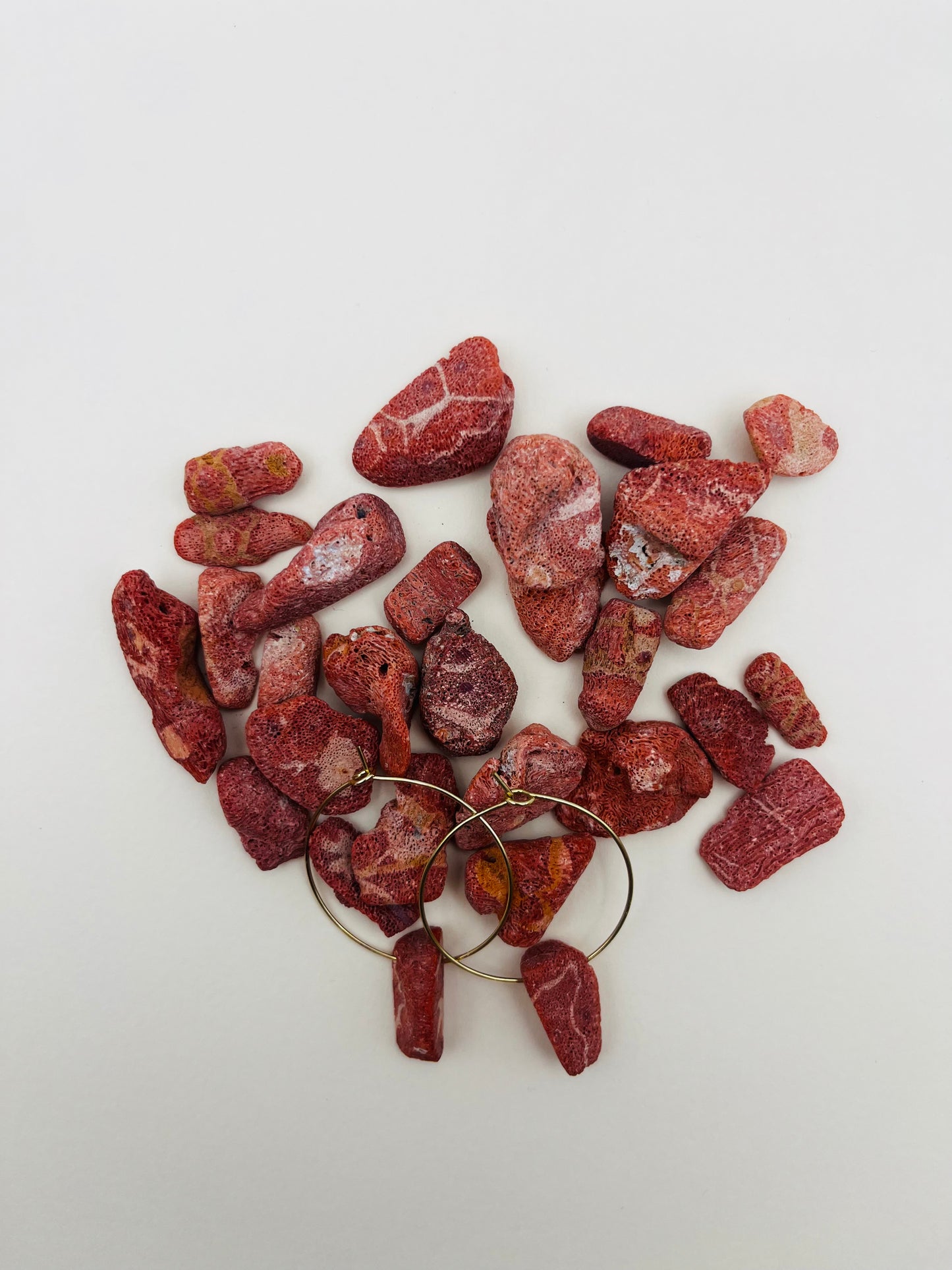 Pendientes Peñón – pendientes con aro dorado fino y piezas de coral rojo natural rugoso, semiocultos entre una gran cantidad de trozos de coral rojo natural de distintas formas y tamaños, sobre fondo blanco, hechos a mano en Murcia
