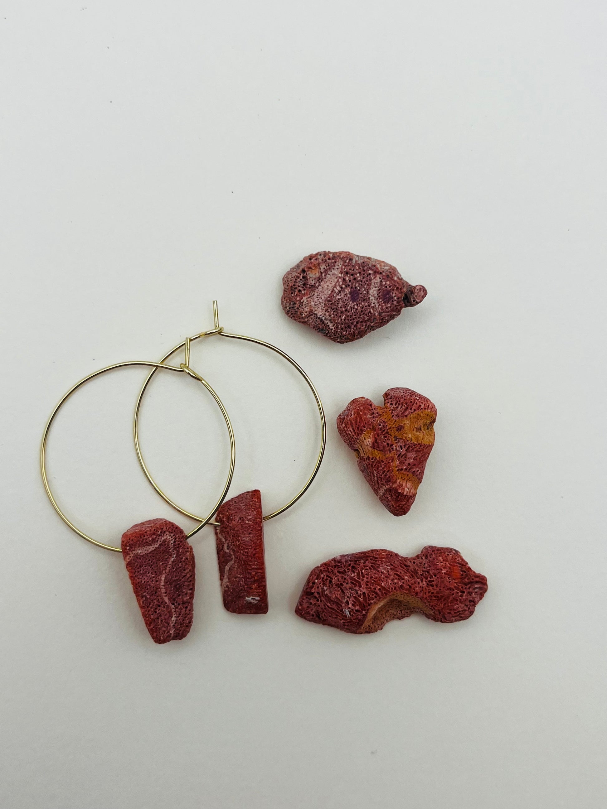 Pendientes Peñón – pendientes con aro dorado fino y dos piezas de coral rojo natural rugoso, con trozos de coral rojo natural sueltos esparcidos, sobre fondo blanco, hechos a mano en Murcia