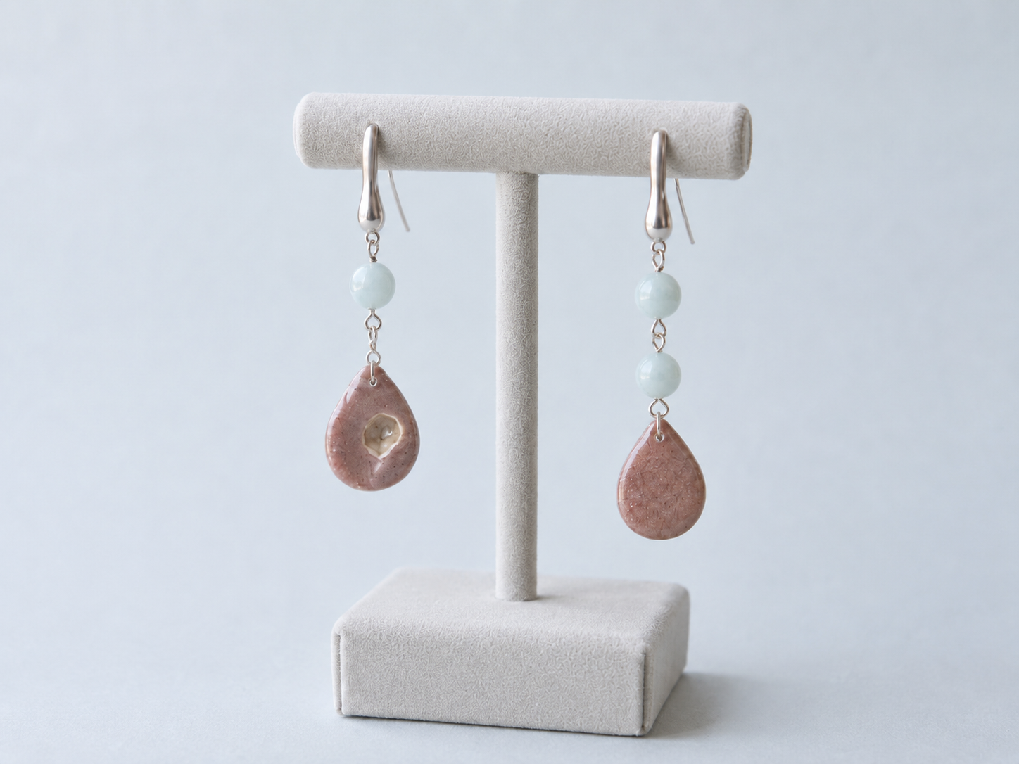 Par de pendientes artesanales Periwinkle sobre expositor de joyería, con perlas nacaradas iridiscentes en forma de gota y cuentas de piedra azul, montados en acero inoxidable y mostrando el diseño asimétrico de ambas piezas.
