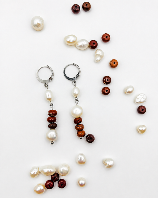 Pendientes de Cuadratura Studio con aro plateado, perla barroca blanca y cuentas de jaspe rojo, rodeados de perlas barrocas y cuentas de jaspe rojo sueltas sobre fondo blanco. Montados a mano en Murcia.`