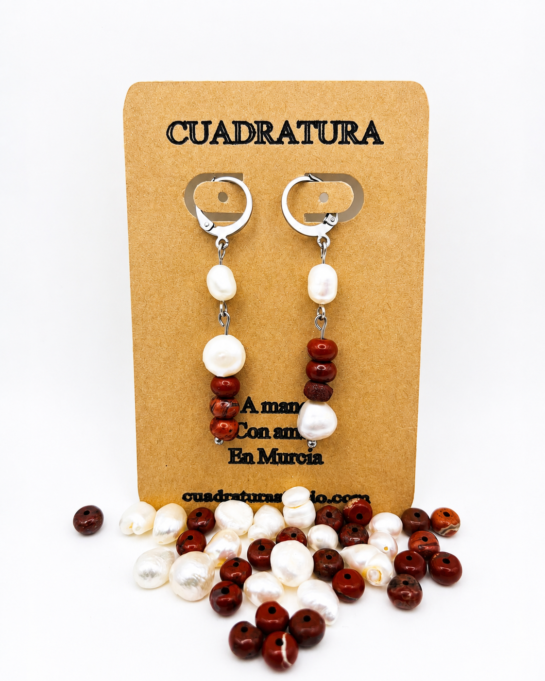 Pendientes asimétricos de Cuadratura Studio en tarjeta kraft: aro plateado con dos perlas barrocas blancas, y aro con perla barroca, cuentas de jaspe rojo y segunda perla, rodeados de perlas y jaspe rojo sueltos. Montados a mano en Murcia.`