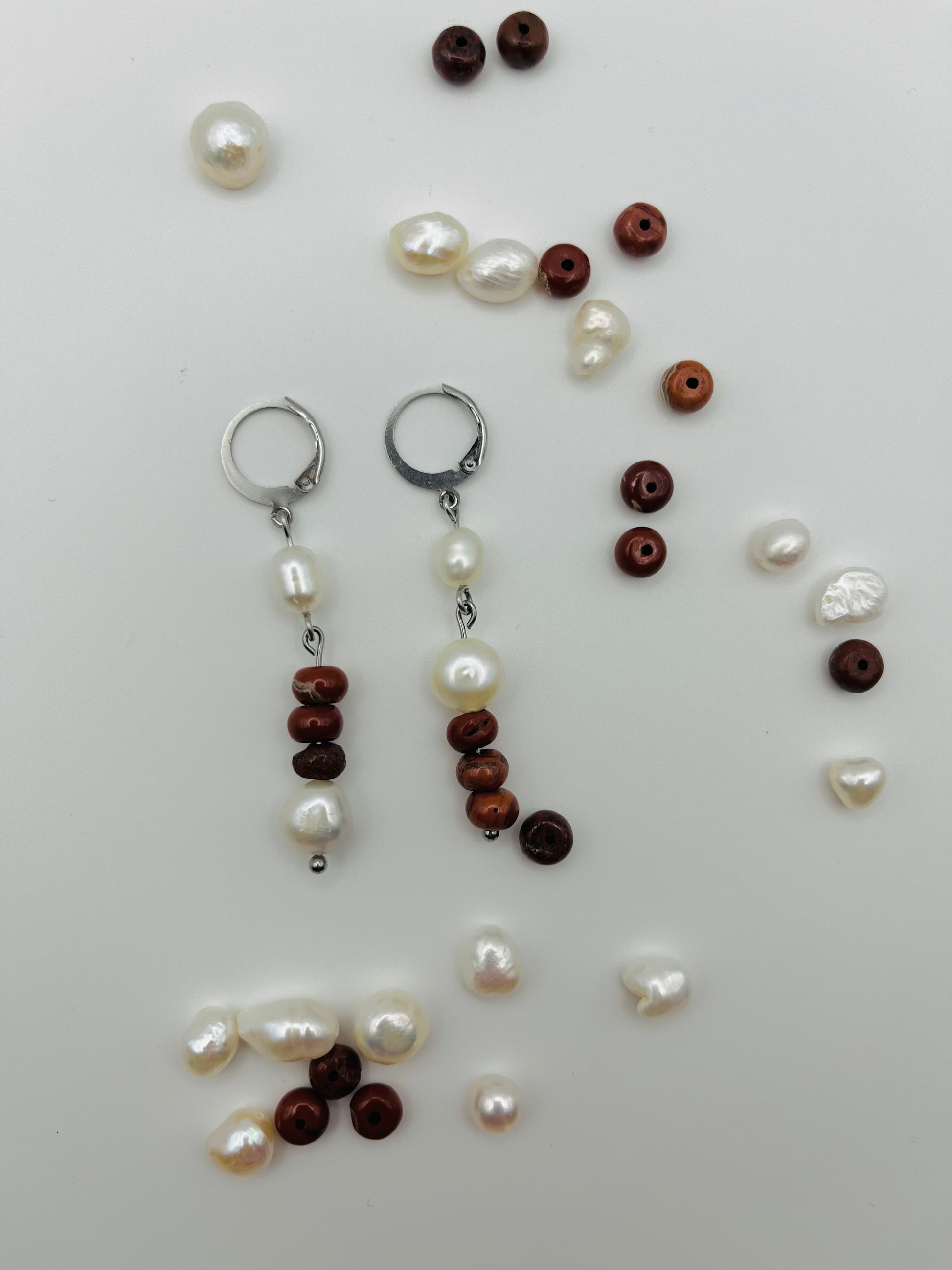 Pendientes Pleamar – dos enganches plateados tipo palanca con perla oval blanca, tres cuentas redondas de jaspe rojo oscuro y perla oval blanca en la base, con perlas oval blancas y cuentas de jaspe rojo sueltas esparcidas, fondo blanco, hechos a mano en Murcia