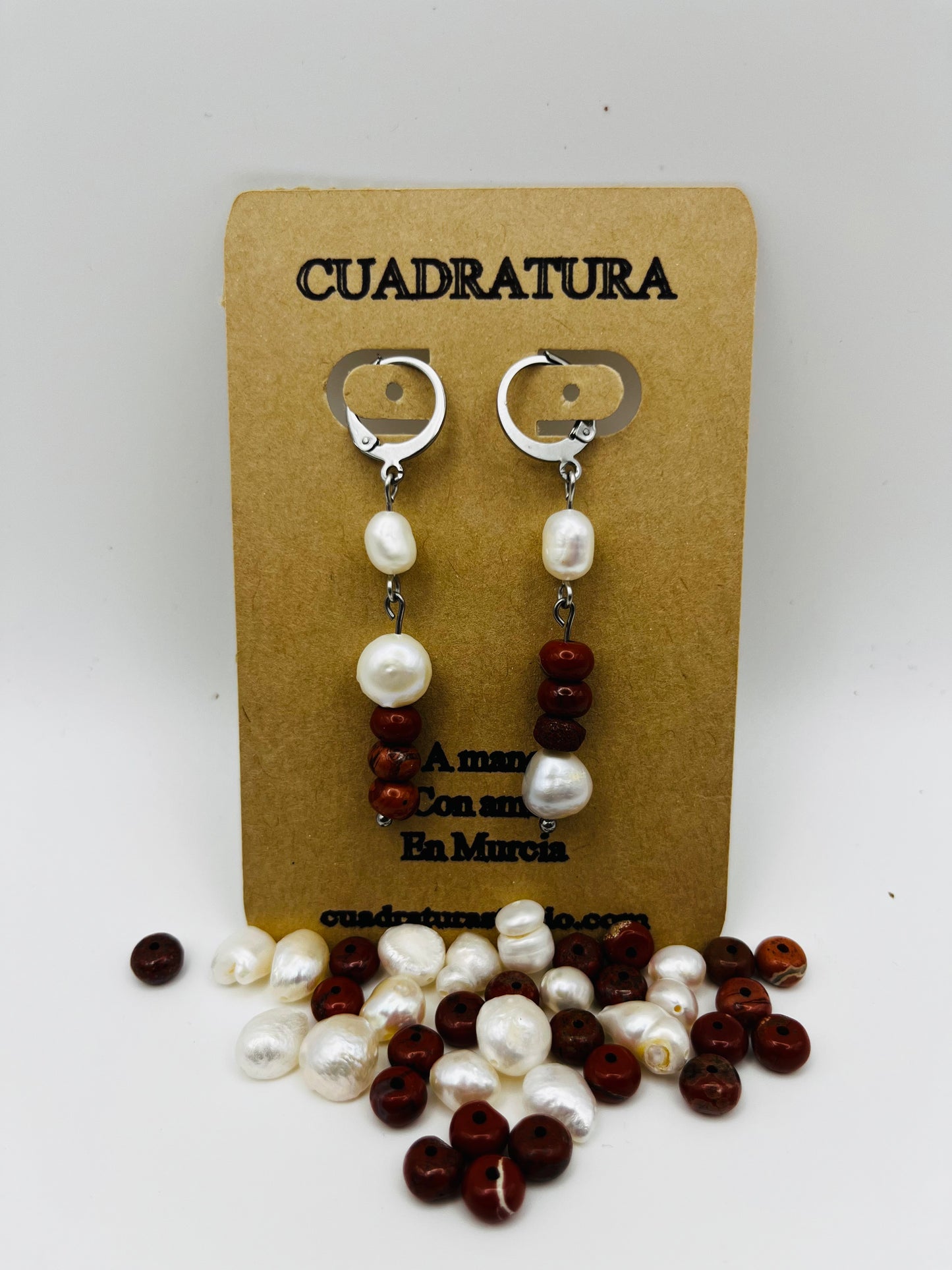 Pendientes Pleamar – pendientes simétricos con enganche plateado tipo palanca, perla oval blanca, tres cuentas redondas de jaspe rojo oscuro y perla oval blanca en la base, en tarjeta Cuadratura, fondo blanco, con perlas oval blancas y cuentas de jaspe rojo sueltas en la base, hechos a mano en Murcia