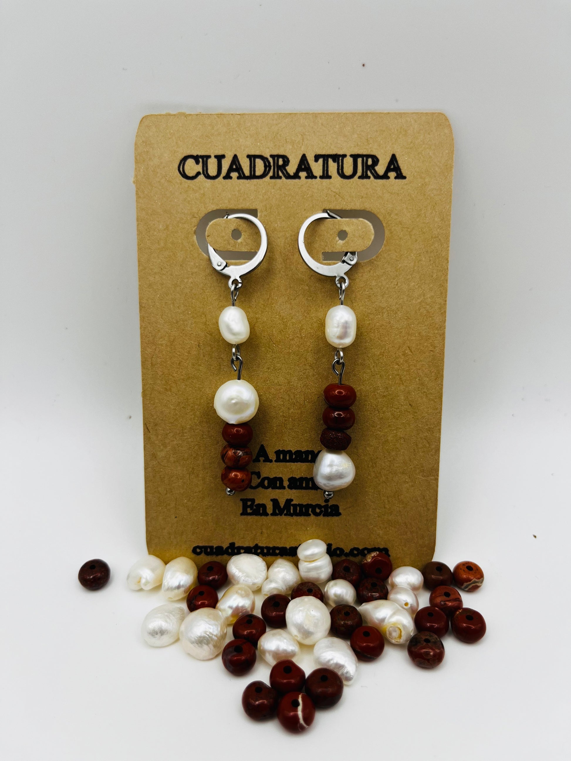 Pendientes Pleamar – pendientes simétricos con enganche plateado tipo palanca, perla oval blanca, tres cuentas redondas de jaspe rojo oscuro y perla oval blanca en la base, en tarjeta Cuadratura, fondo blanco, con perlas oval blancas y cuentas de jaspe rojo sueltas en la base, hechos a mano en Murcia