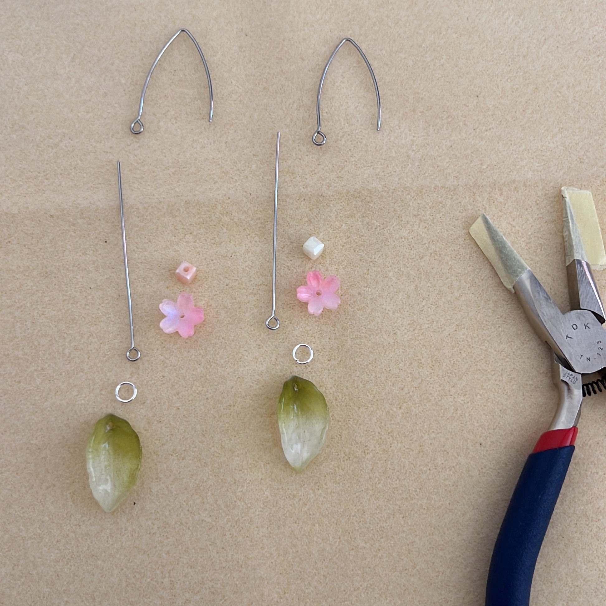 Componentes de los pendientes Primavera dispuestos para su elaboración artesanal, con hojas de jade tallado, flores de cristal rosa y cierres plateados.