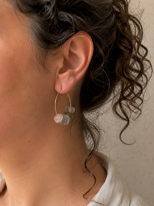 Pendientes artesanales Toulouse sobre modelo, con aros de acero inoxidable dorado y diseño asimétrico de chips de cuarzo rosa, prehnita y labradorita en tonos rosa y verde grisáceo.