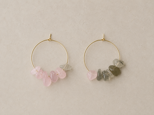 Pendientes artesanales Toulouse con aros de acero inoxidable dorado y diseño asimétrico. Uno combina chips de cuarzo rosa y prehnita, y el otro chips de cuarzo rosa, prehnita y labradorita en tonos rosa y verde grisáceo.