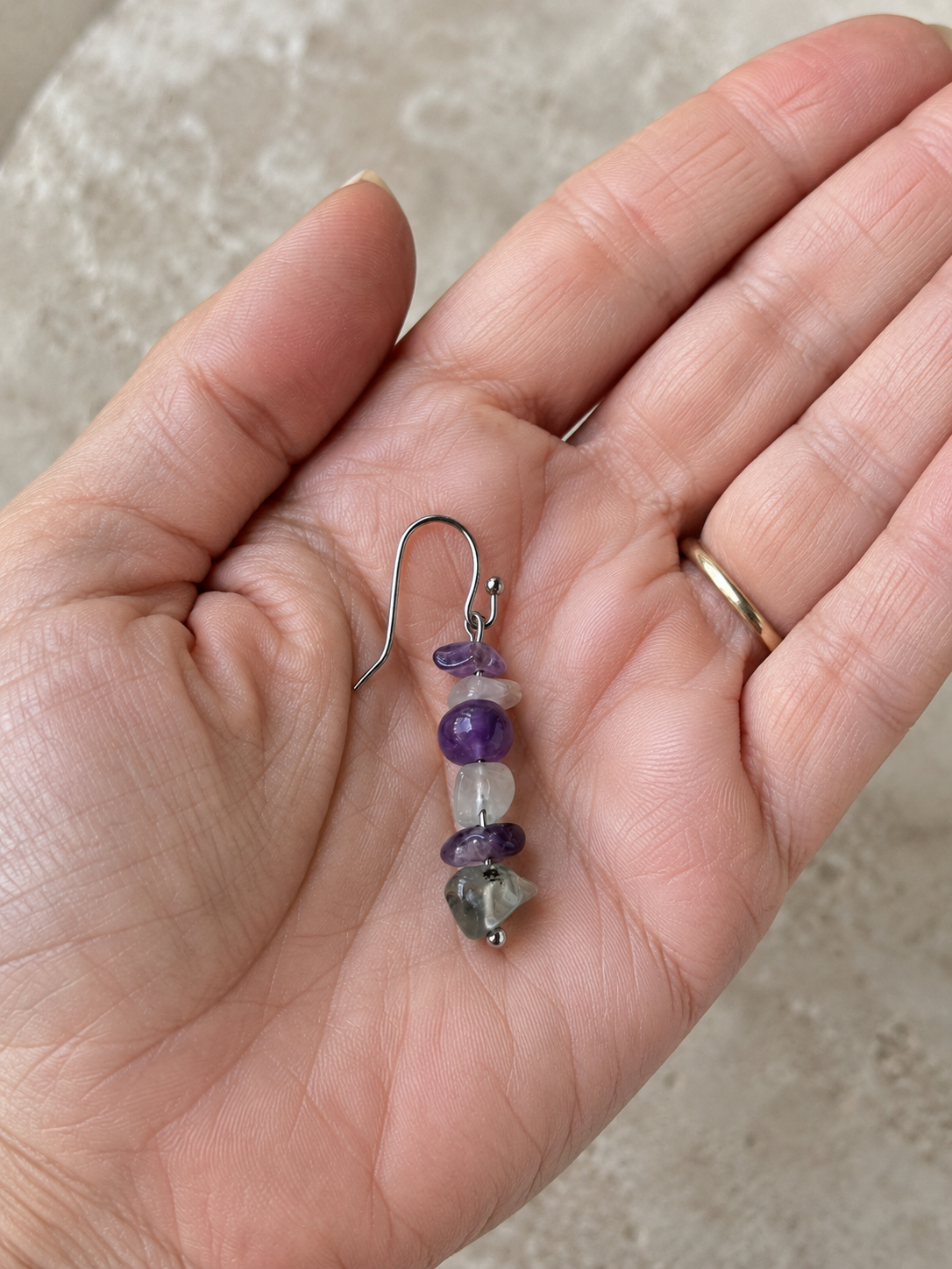Pendiente Verena sobre la palma de una mano, elaborado con amatista y fluorita natural en tonos violeta, blanco y verde, con gancho de acero inoxidable.