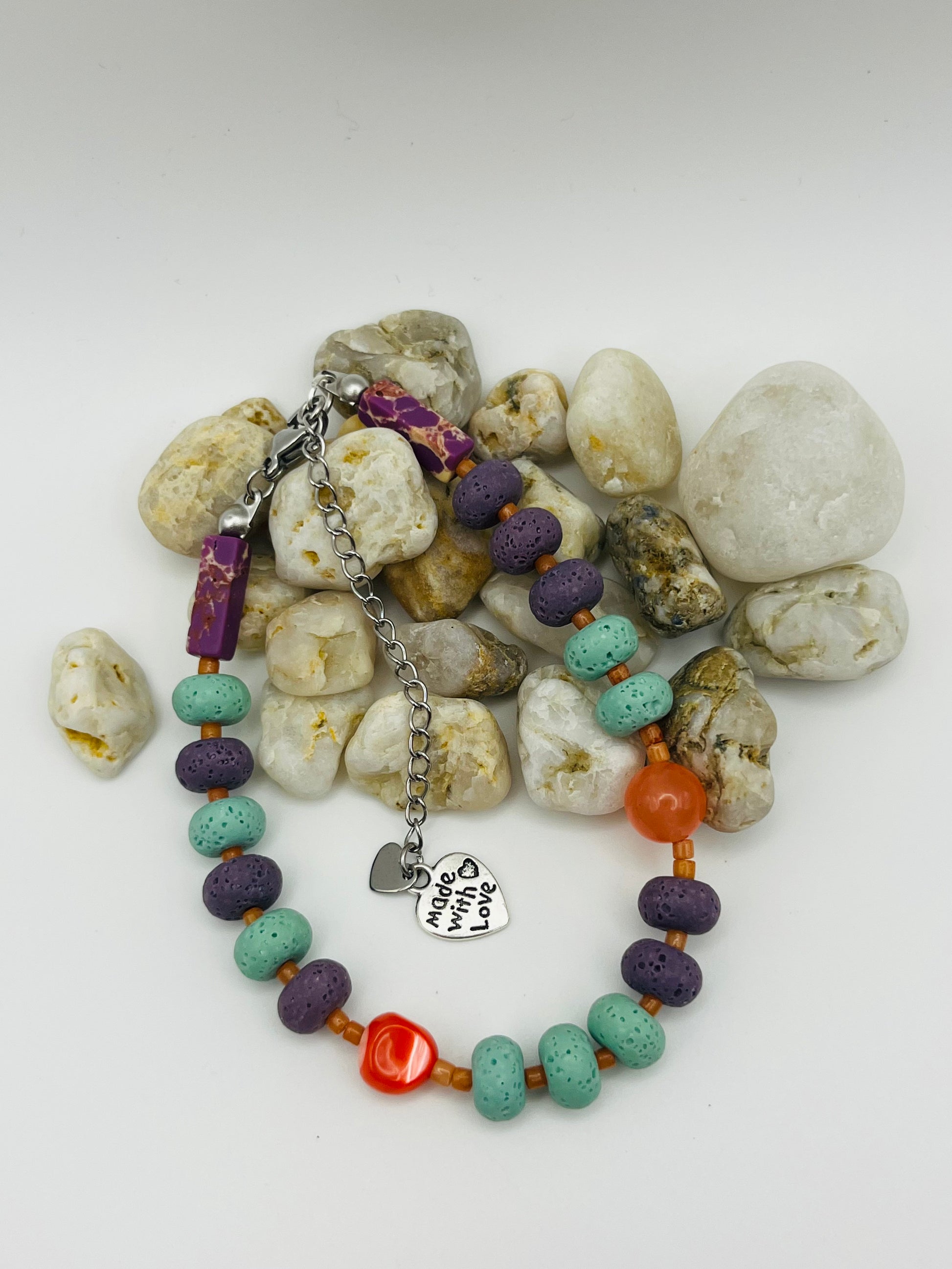 Vista completa de pulsera artesanal Arrecife con lava volcánica turquesa y morada, cornalina naranja, coral rojo y dije corazón plateado, montada a mano en Murcia
