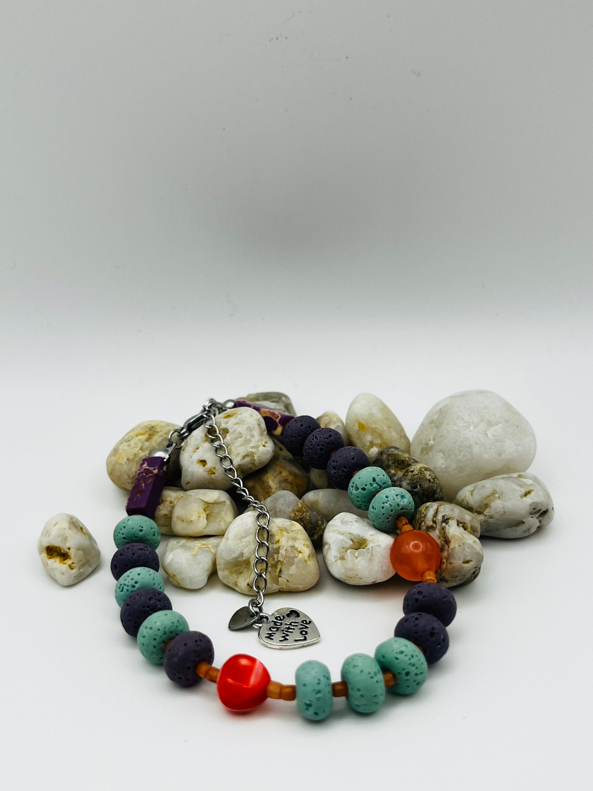 Detalle de pulsera artesanal Arrecife con lava volcánica turquesa y morada, cornalina naranja, coral rojo y dije corazón plateado, montada a mano en Murcia
