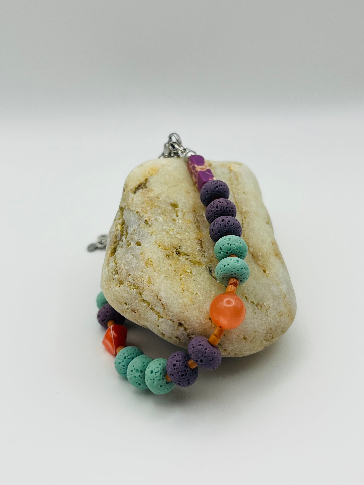 Pulsera artesanal Arrecife sobre piedra, con lava volcánica turquesa y morada, cornalina naranja y coral rojo, montada a mano en Murcia
